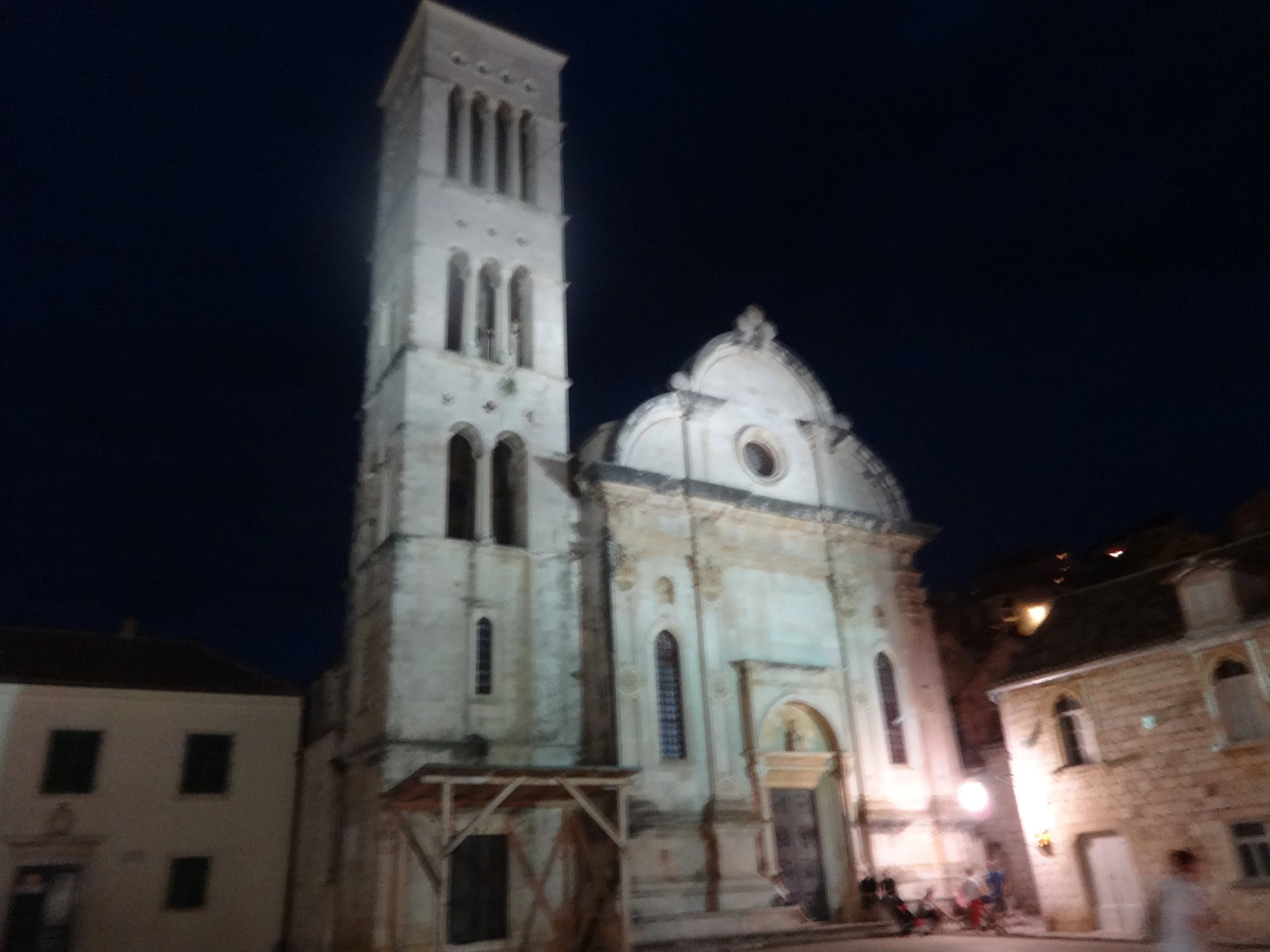 Nighttime view of a historic church with a tall bell tower, ornate architecture, and a rounded dome, illuminated by exterior lighting in a city street.