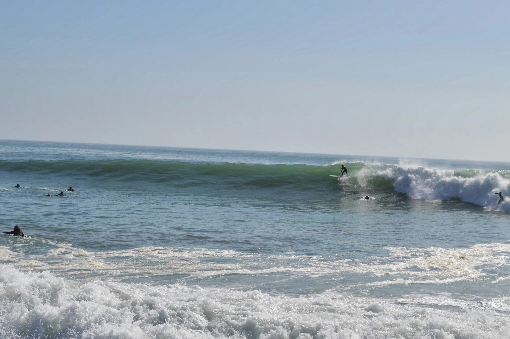 People surfing on ocean waves near the shoreline with clear blue sky in the background.