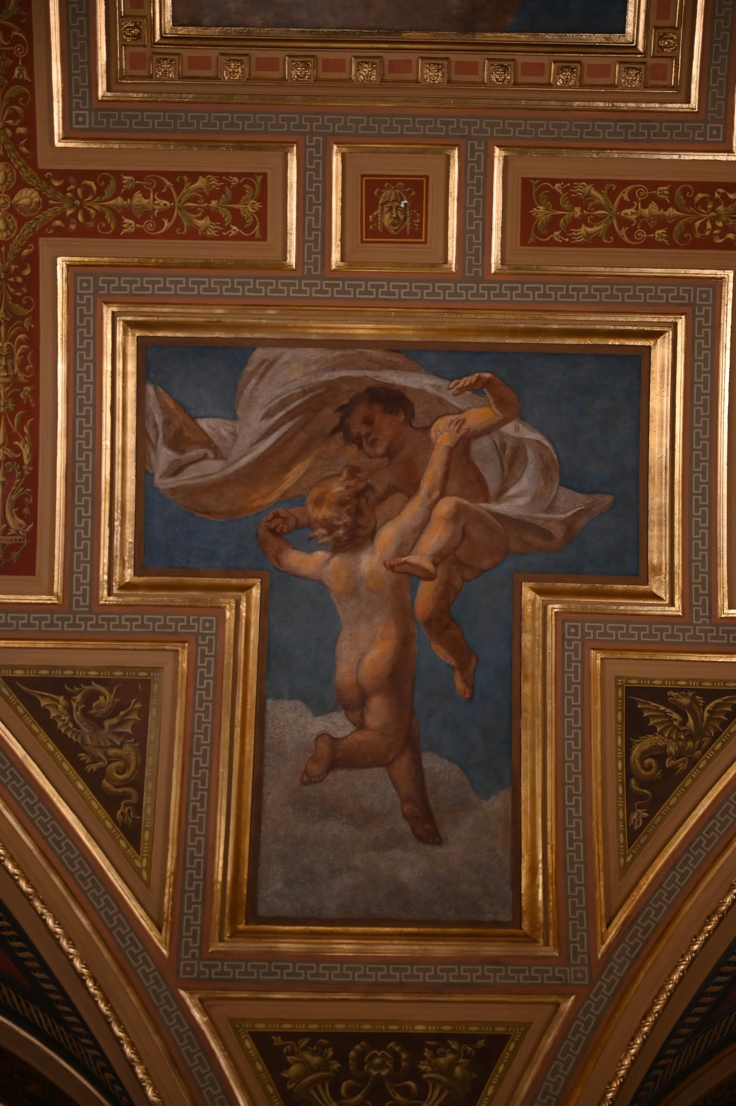 Painting of a man carrying a woman on his shoulders, set in a decorated ceiling with intricate gold and red patterns.