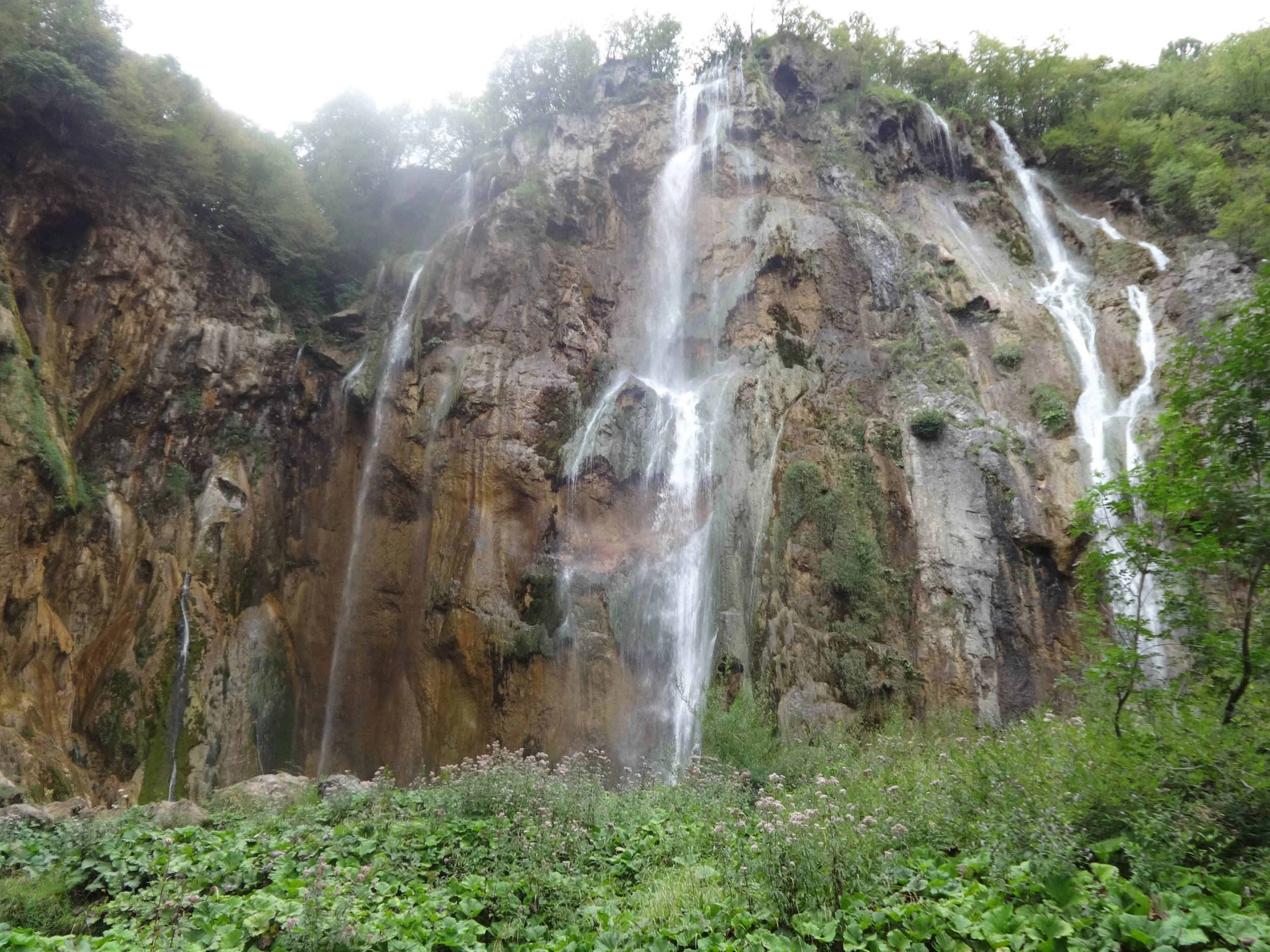 A waterfall cascading down a rocky cliff surrounded by green trees and foliage.