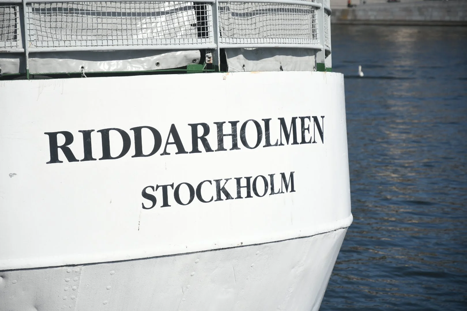 Close-up of a boat's bow with the text 'RIDDARHOLMEN STOCKHOLM' on the side, on a body of water
