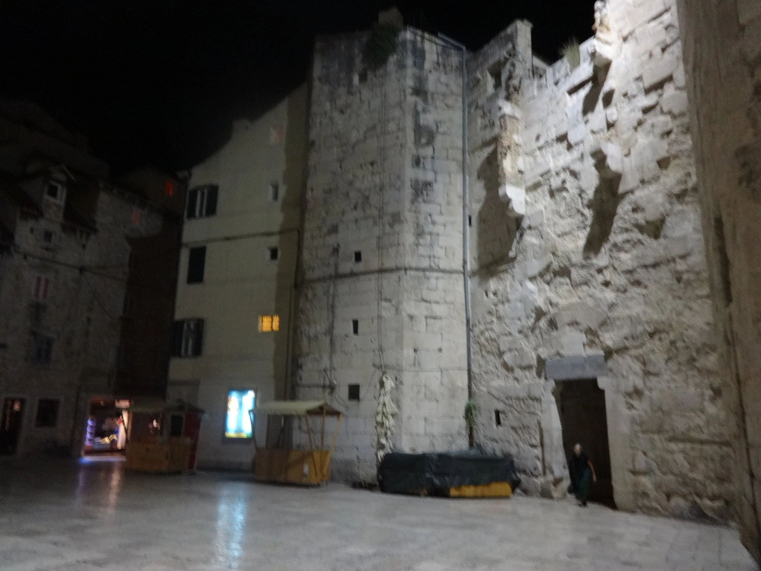 Nighttime image of a partially constructed stone wall with construction scaffolding. Surrounding buildings are visible in the background.