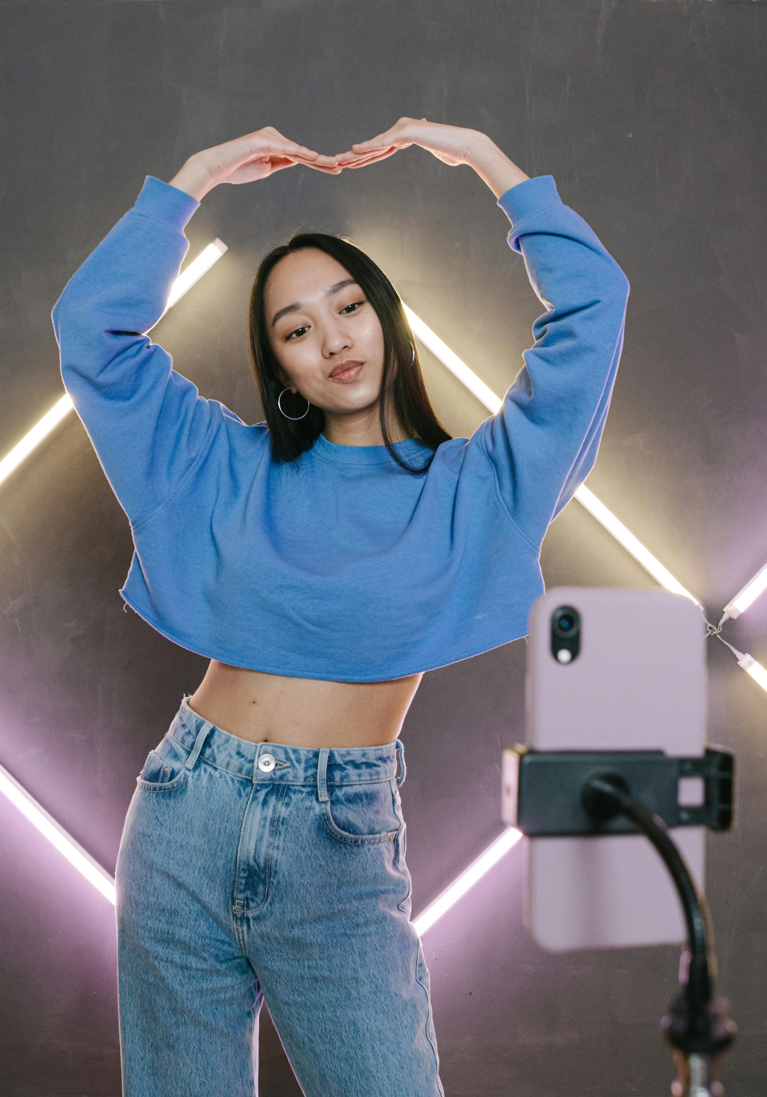 Woman in a blue sweatshirt forming a heart shape with her hands during a mirror selfie