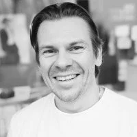 Black-and-white headshot of a smiling man with slicked-back hair wearing a white shirt
