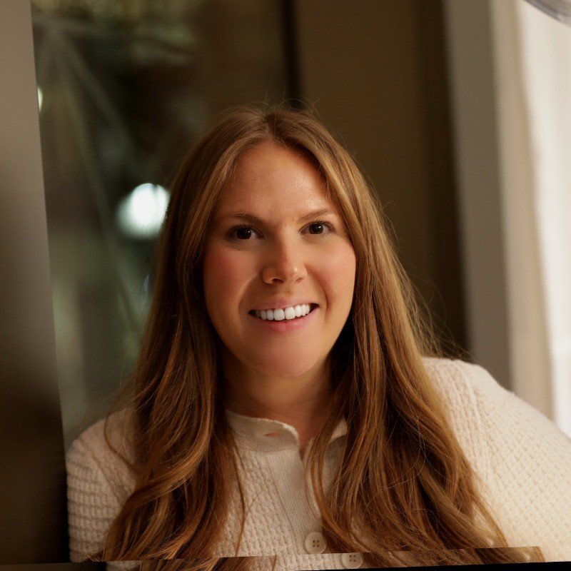 Smiling woman with long brown hair wearing a cream sweater indoors