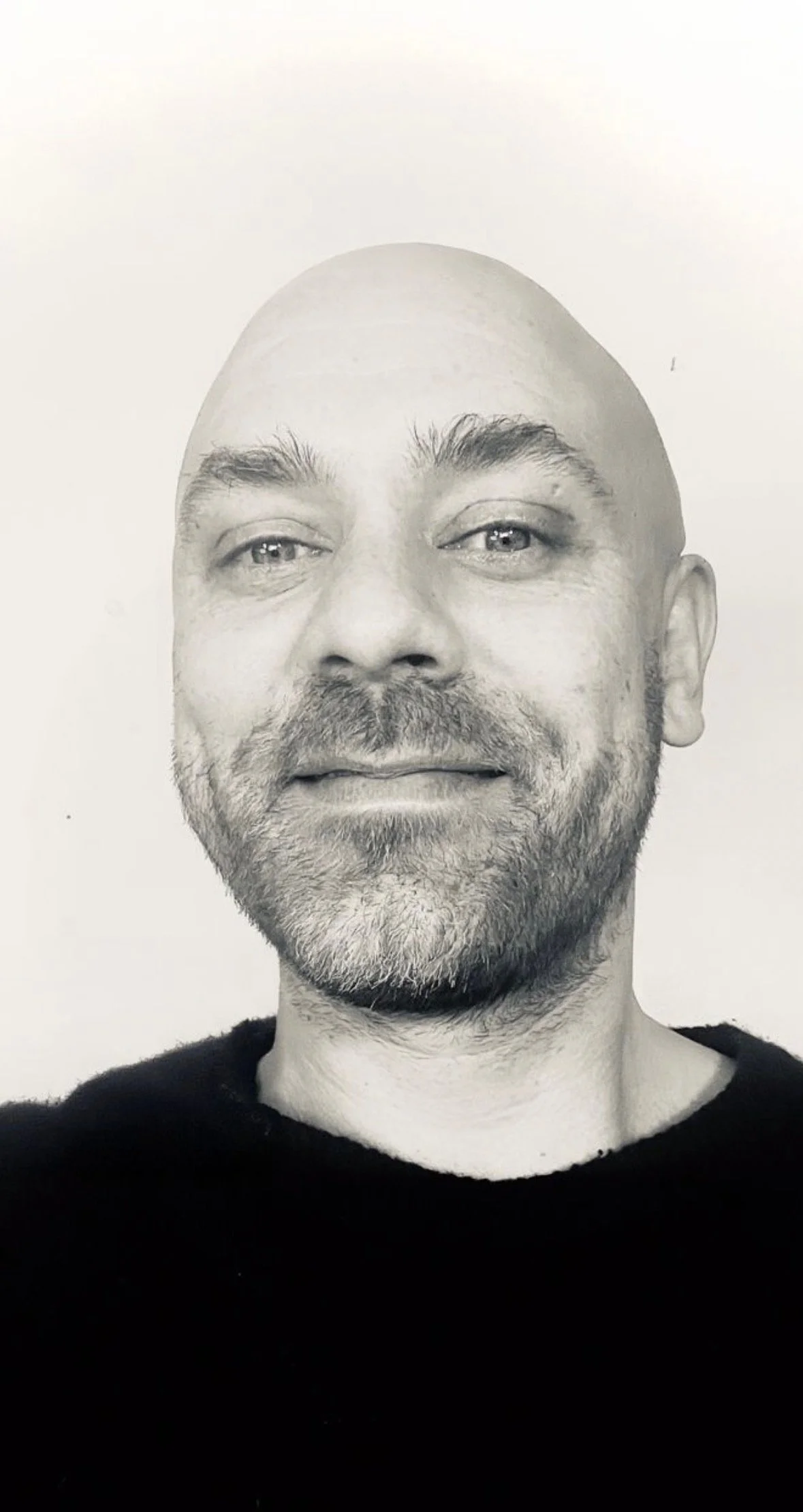 Black-and-white headshot of a bald, bearded man wearing a dark shirt