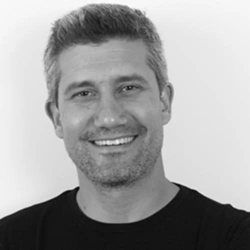 Black-and-white headshot of a smiling man with short hair wearing a black shirt