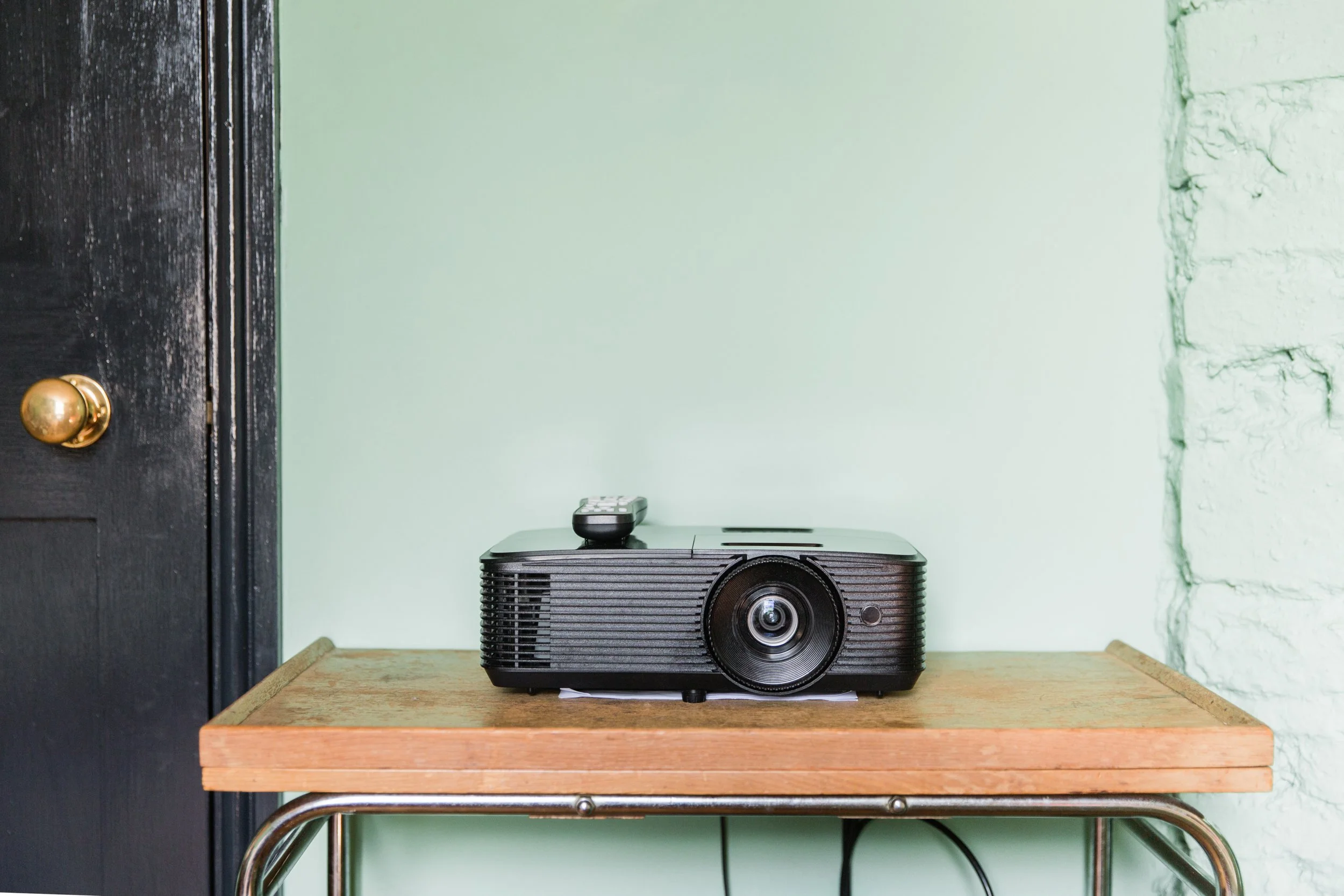 Black projector placed on a wooden table against a light green wall with a textured edge.