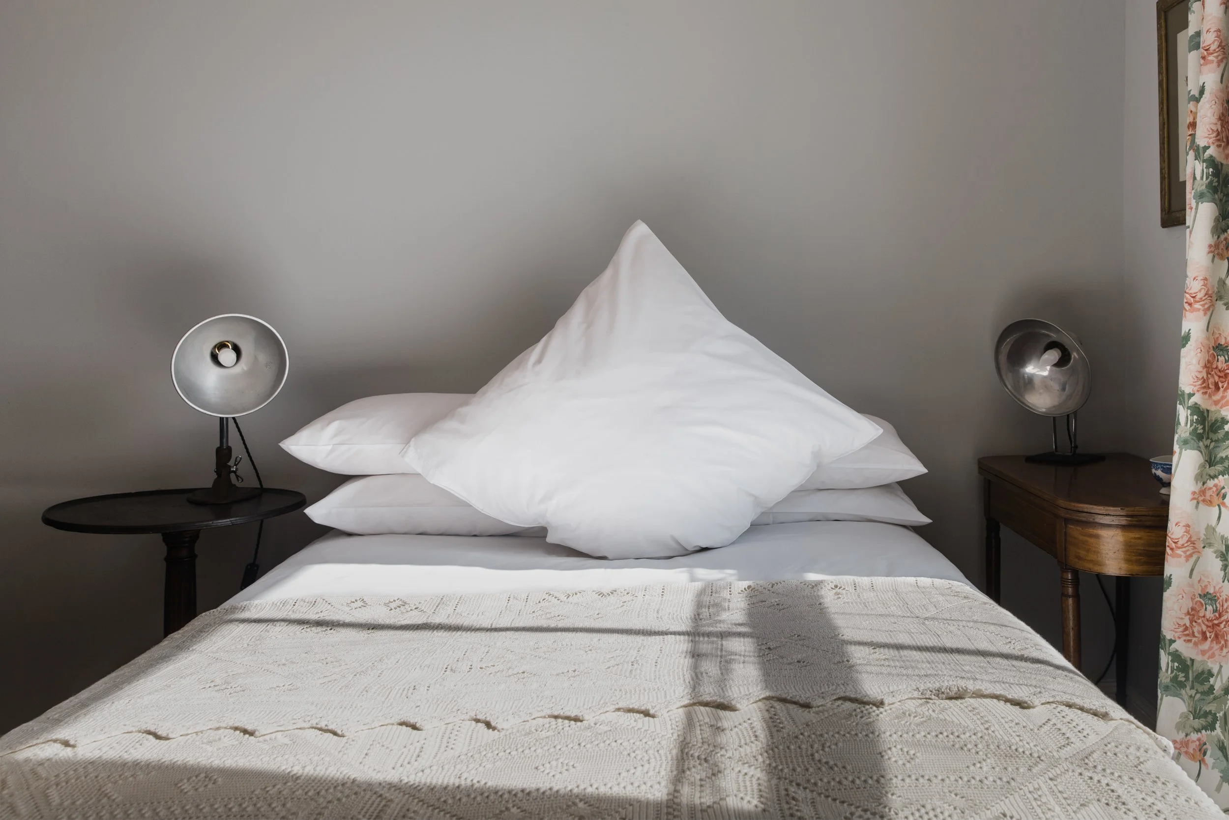 A neatly made bed with white pillows and a crocheted bedspread in a bedroom with side tables on either side, each holding a vintage-style lamp.
