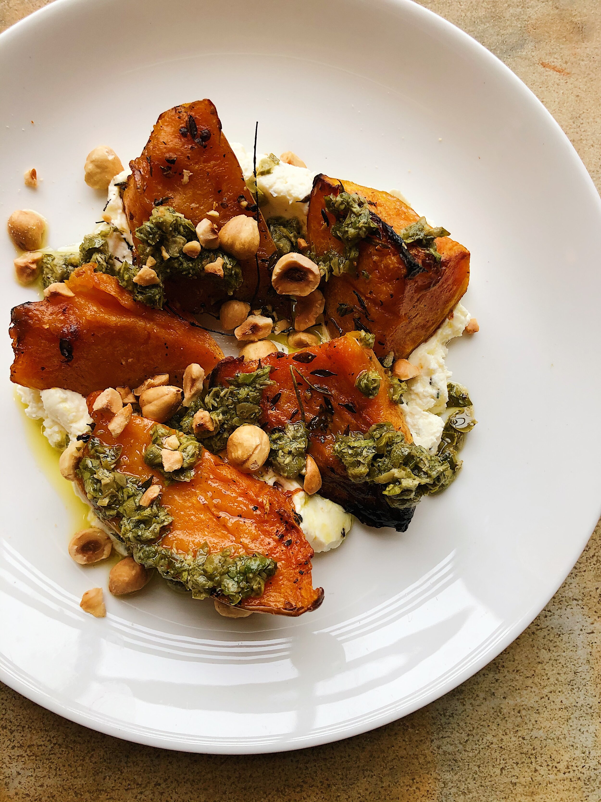 Baked sweet potatoes topped with chopped nuts and herbs, served on a bed of creamy white sauce on a white plate.
