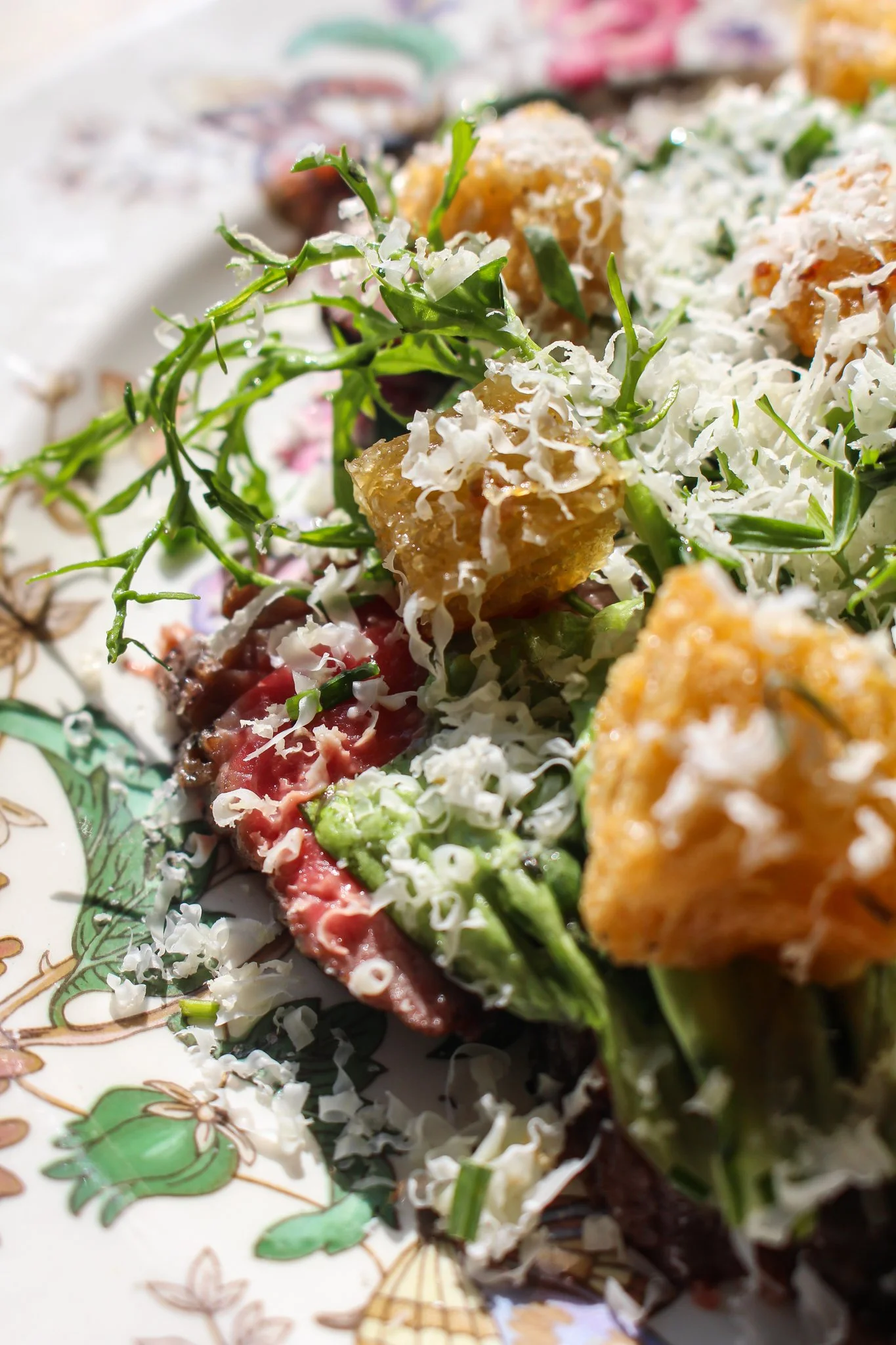 Close-up of a plate with assorted salads, including greens, shredded cheese, and small breaded fried items.