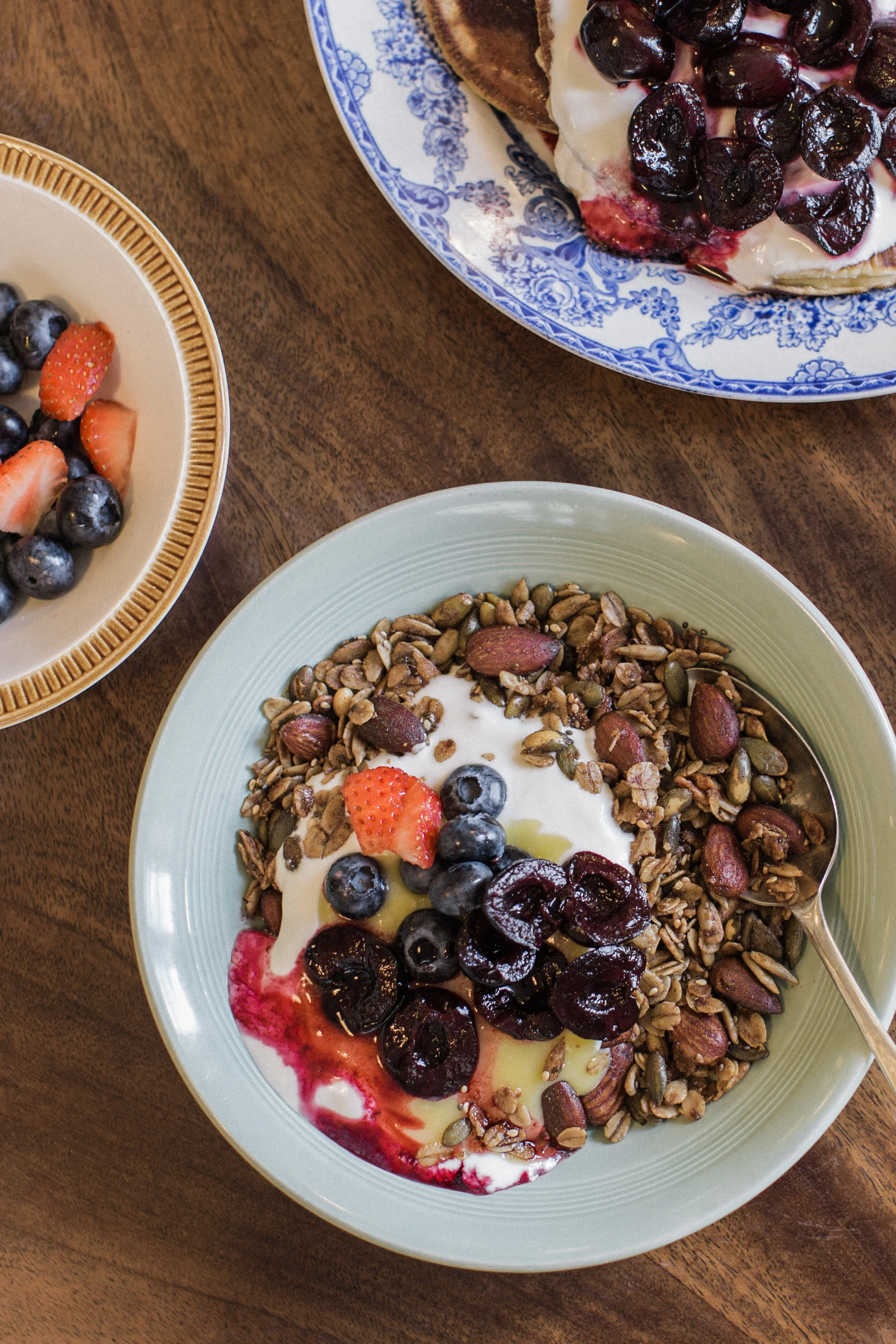 A bowl of yogurt topped with fresh blueberries, strawberries, and cherries, served with granola and almonds on the side.