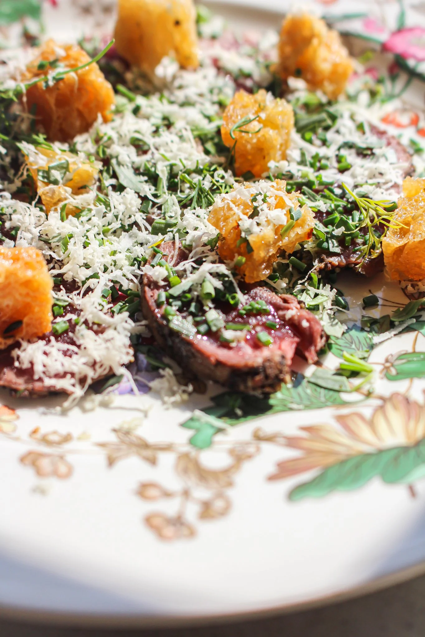 Close-up of a plate with fried foods, grated cheese, herbs, and vegetables, featuring chunks of fried snack with golden-brown exterior.