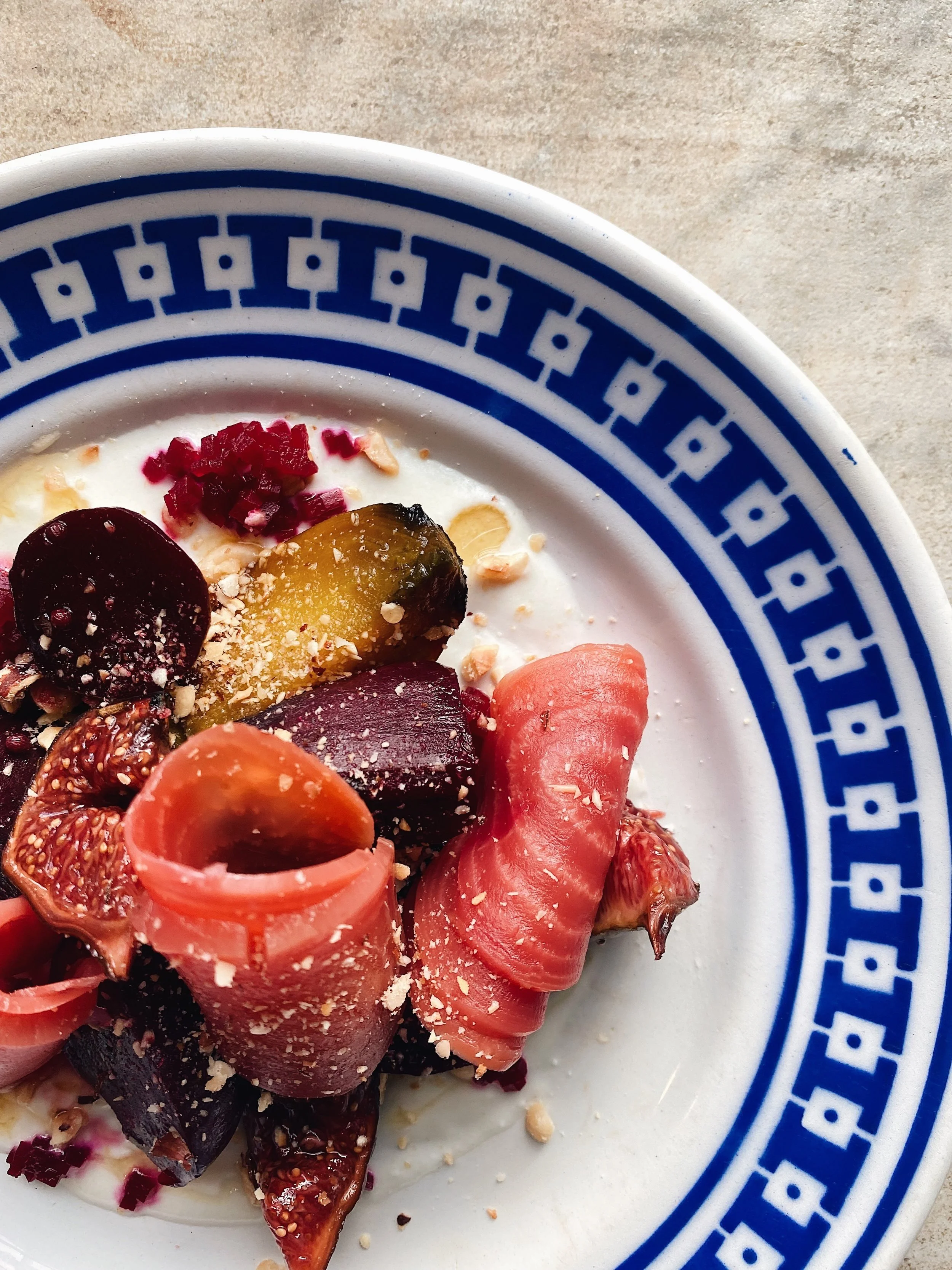 Close-up of a bowl with a decorative blue pattern containing assorted fruit slices and toppings on a beige surface.