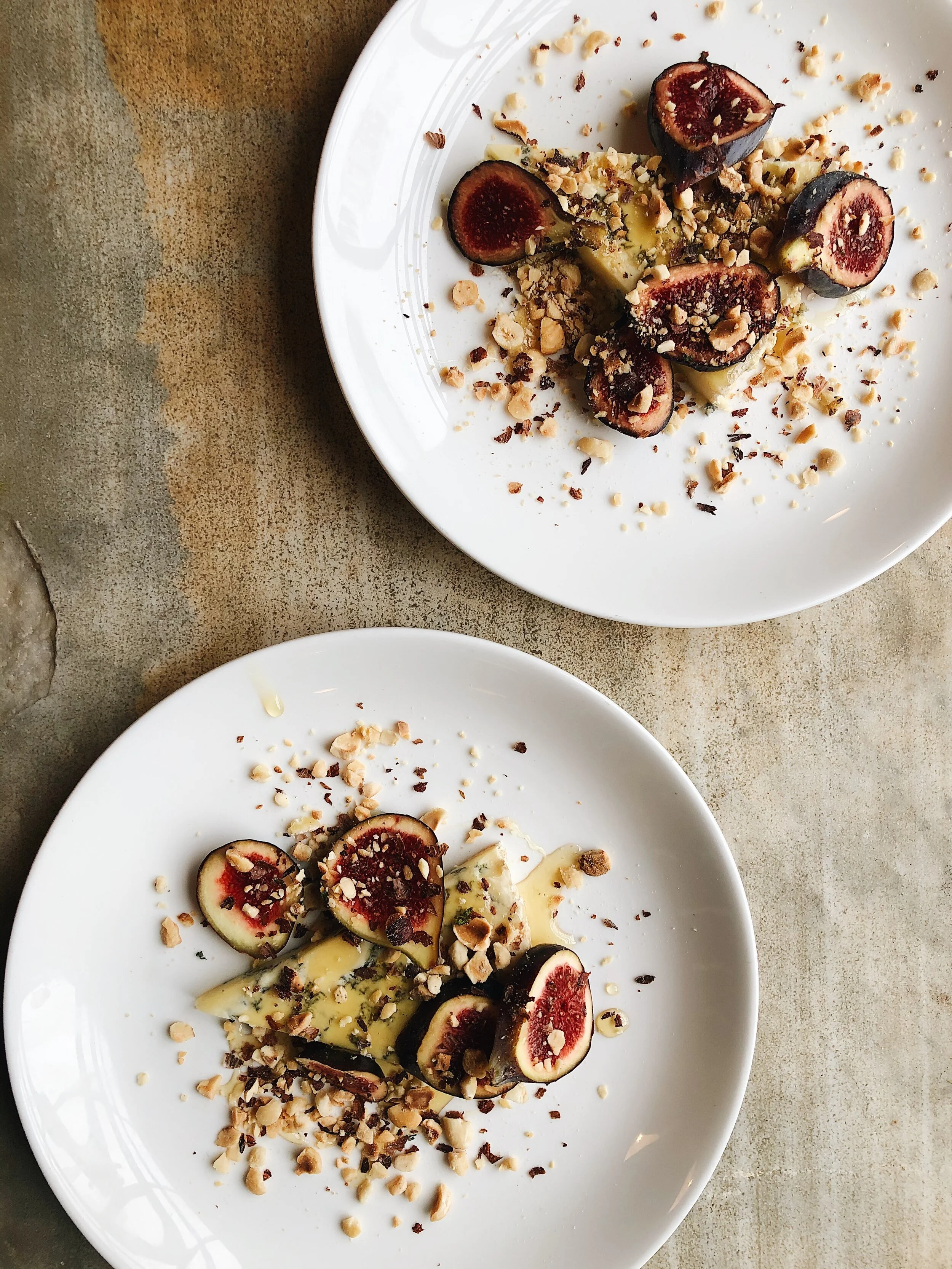 Close-up of a white plate with stuffed figs topped with chopped nuts, drizzled with honey, on a rustic surface.