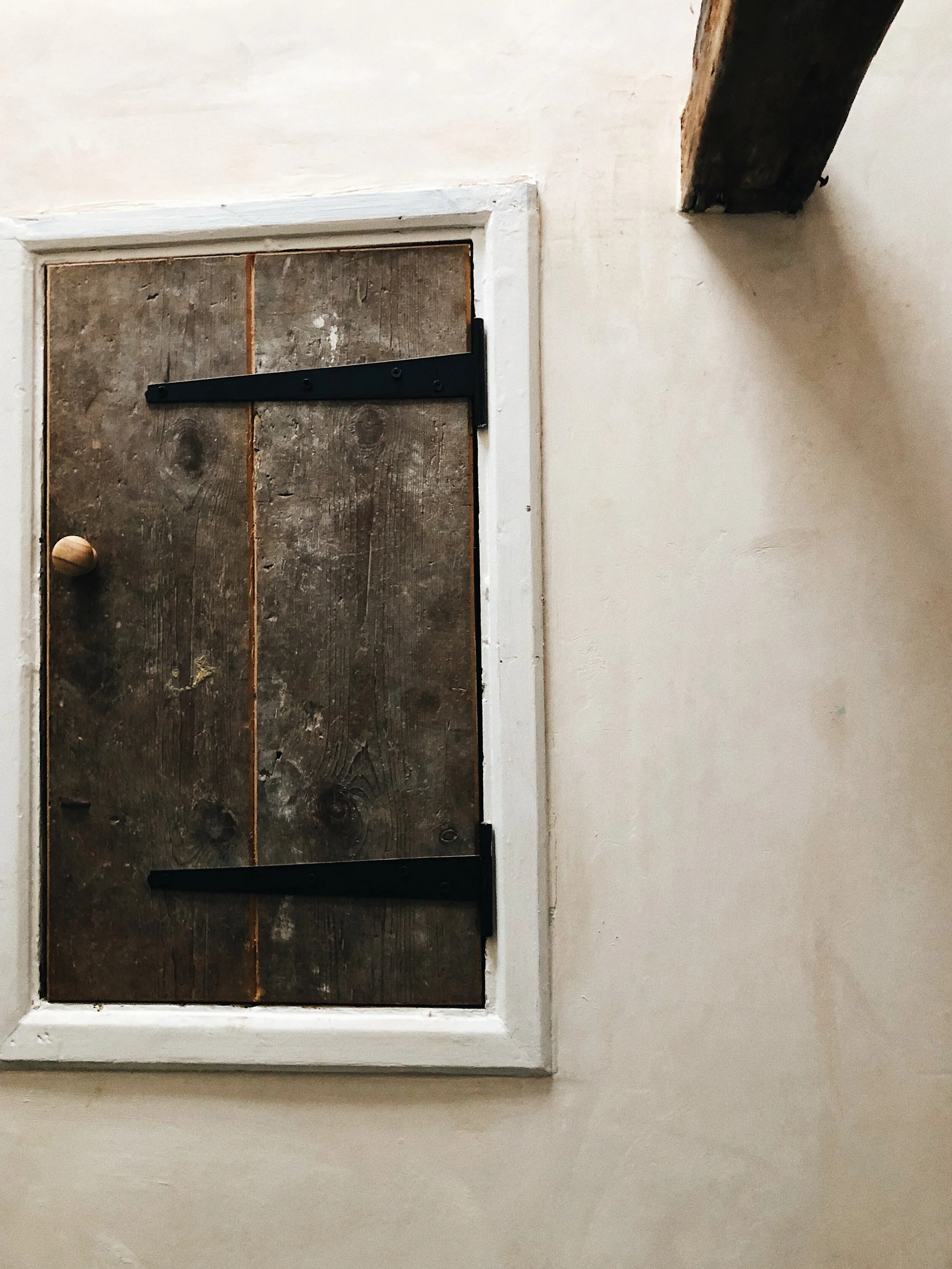 Close-up of a wooden door with black metal hinges and a wooden doorknob, set in a white frame against a white wall.