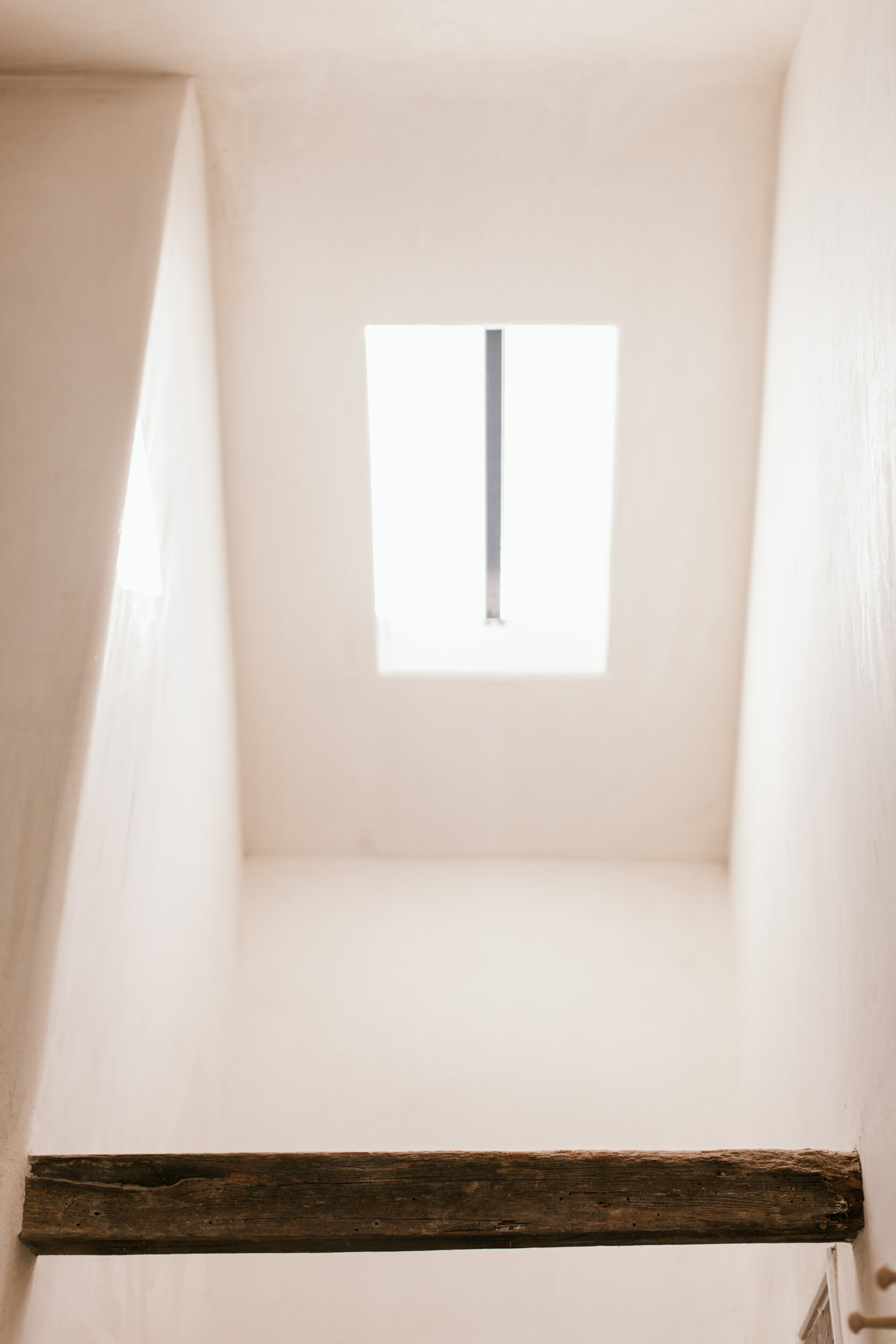 Looking up from an interior space through a square opening in the ceiling, with a view of the sky and a vertical metal bar in the center.