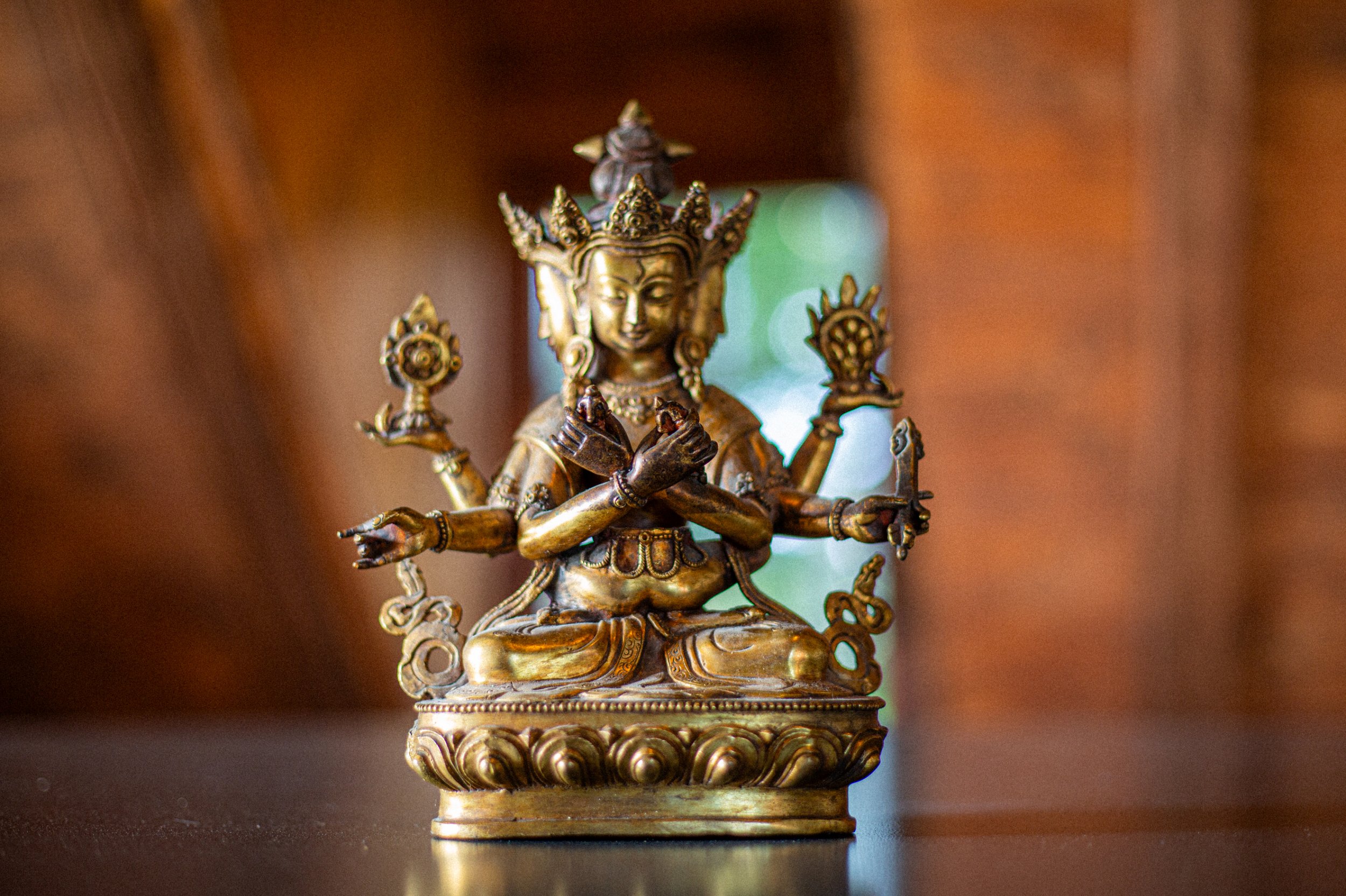 A detailed bronze statue of a multi-armed deity, seated on a decorated base with a serene facial expression, set against a blurred background.
