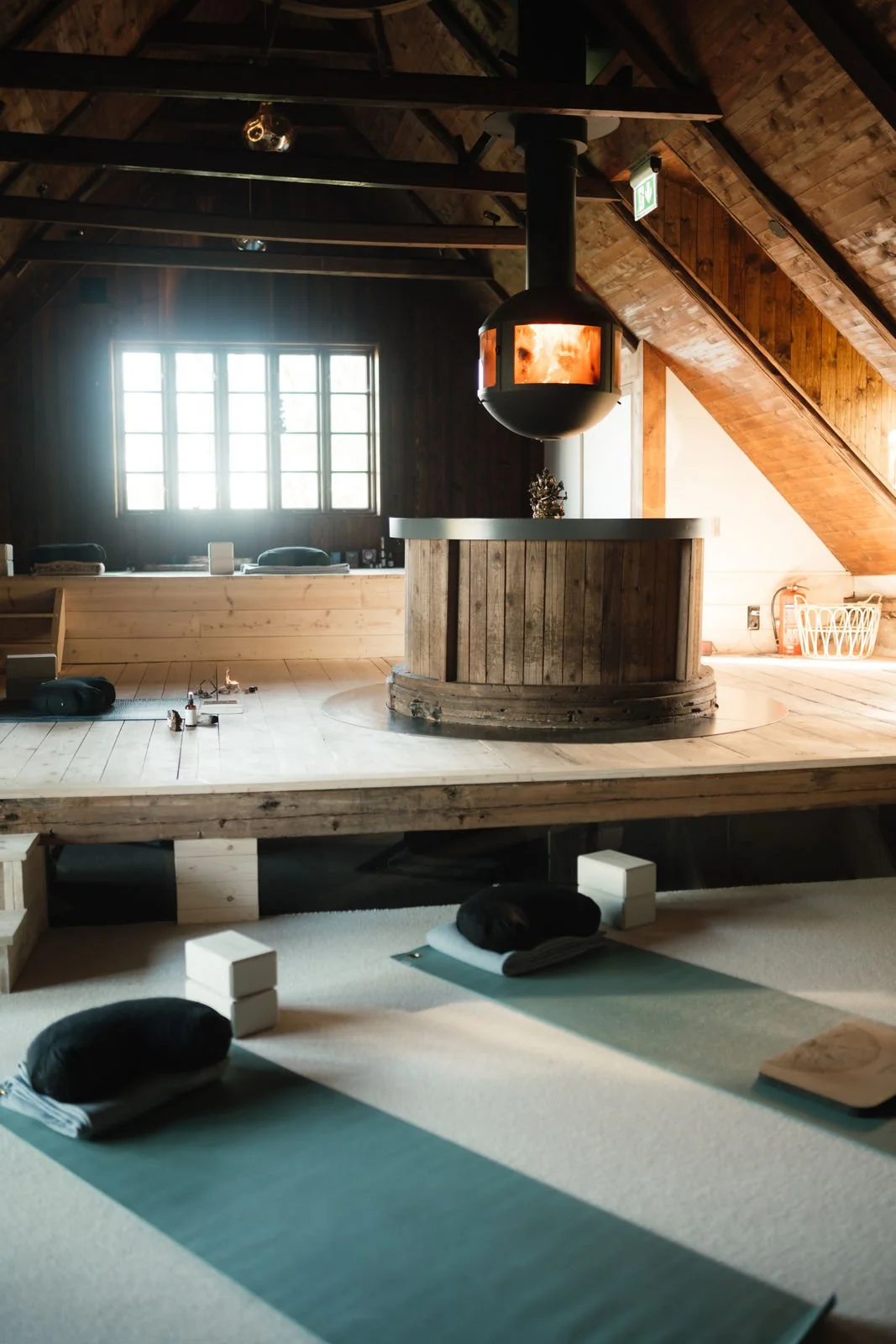 Interior view of a room with wooden walls and ceiling, a large window with views of greenery, a black dome-shaped hanging fireplace, and a small decorative sculpture on a curved wooden counter.