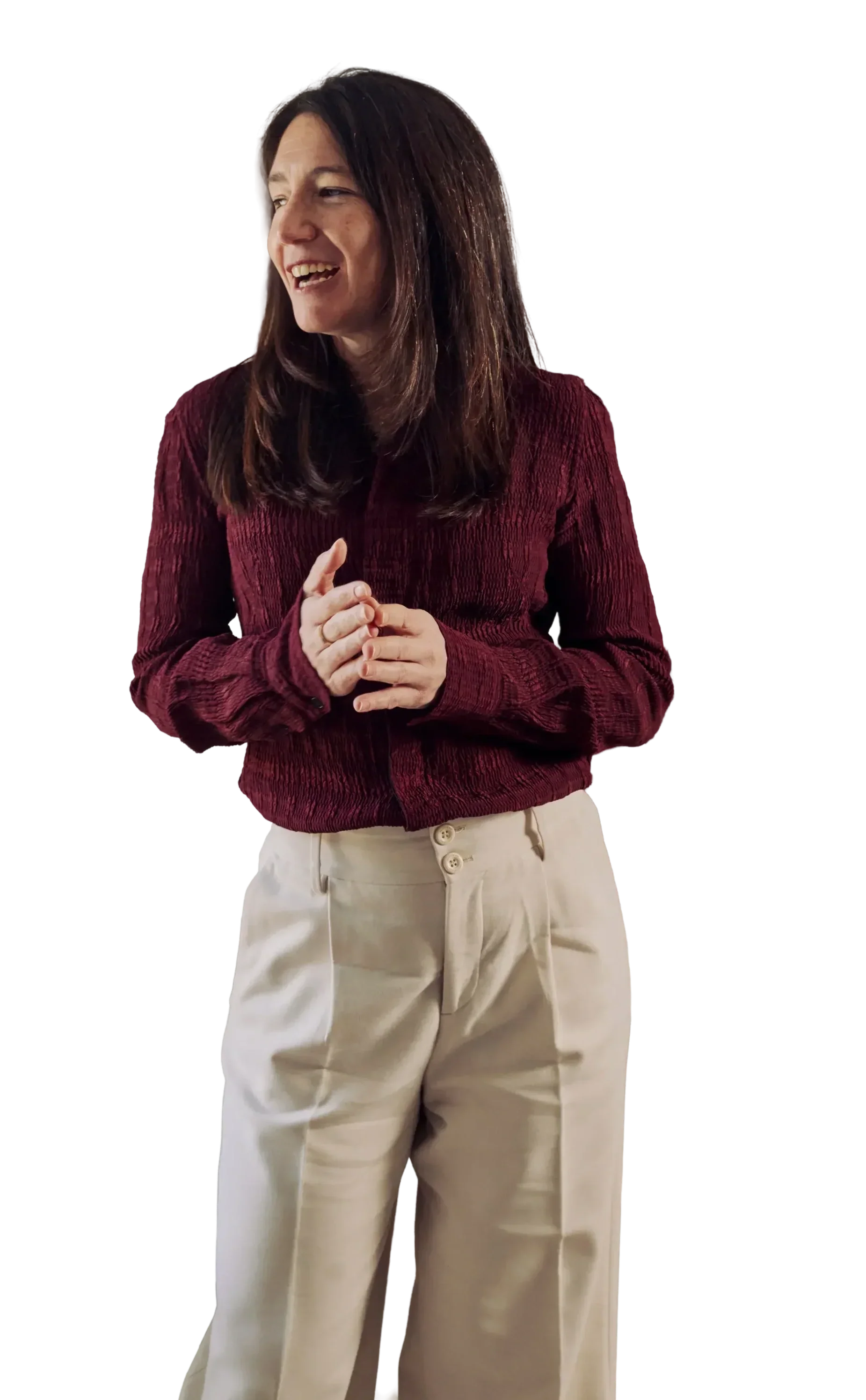 A woman with brown hair wearing a maroon textured sweater and beige wide-leg pants, smiling and clasping her hands.