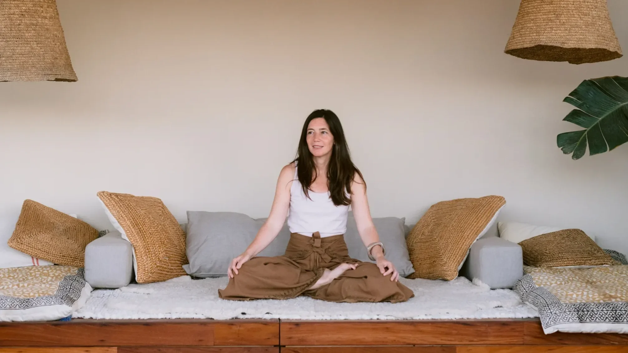 Ana Estrada, women's leadership coach, sitting cross-legged in quiet reflection under woven pendant lights.