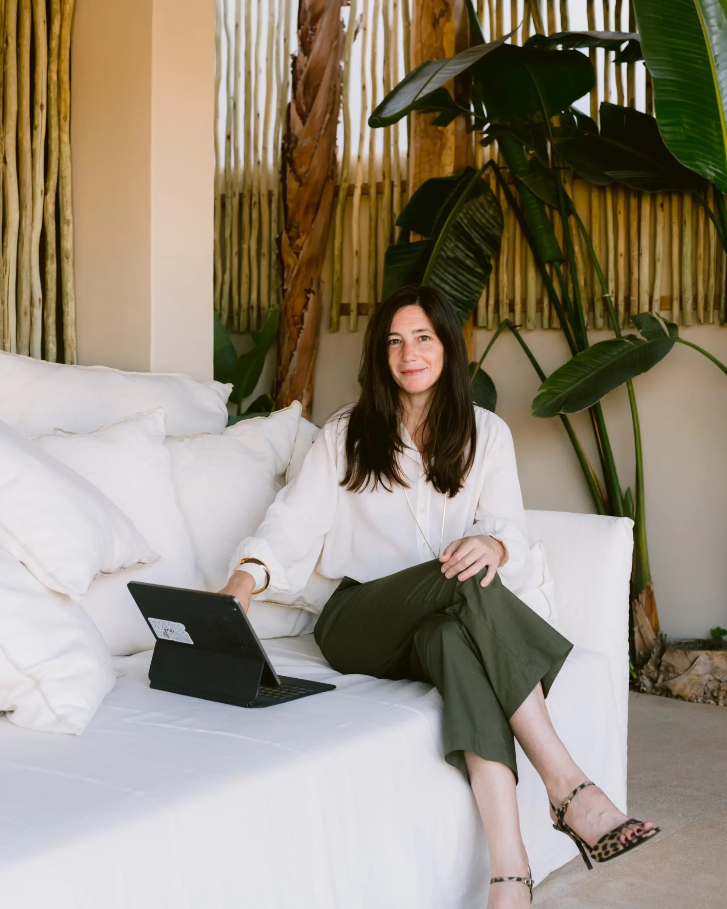 Ana Estrada, executive coach for women, working from a laptop on an outdoor terrace surrounded by tropical plants.