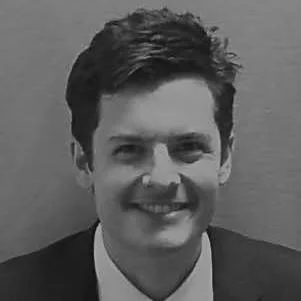 Black and white photo of a young man with dark hair, smiling, wearing a suit and tie.