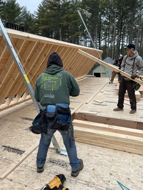 Construction workers installing wooden framing on a building under construction in a wooded area.