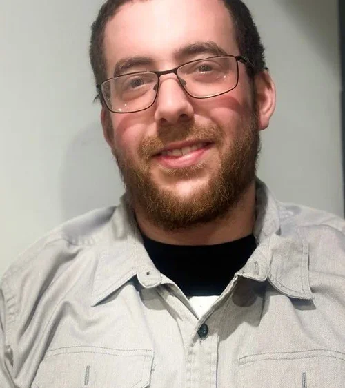 A man with glasses, a beard, and short dark hair smiling at the camera