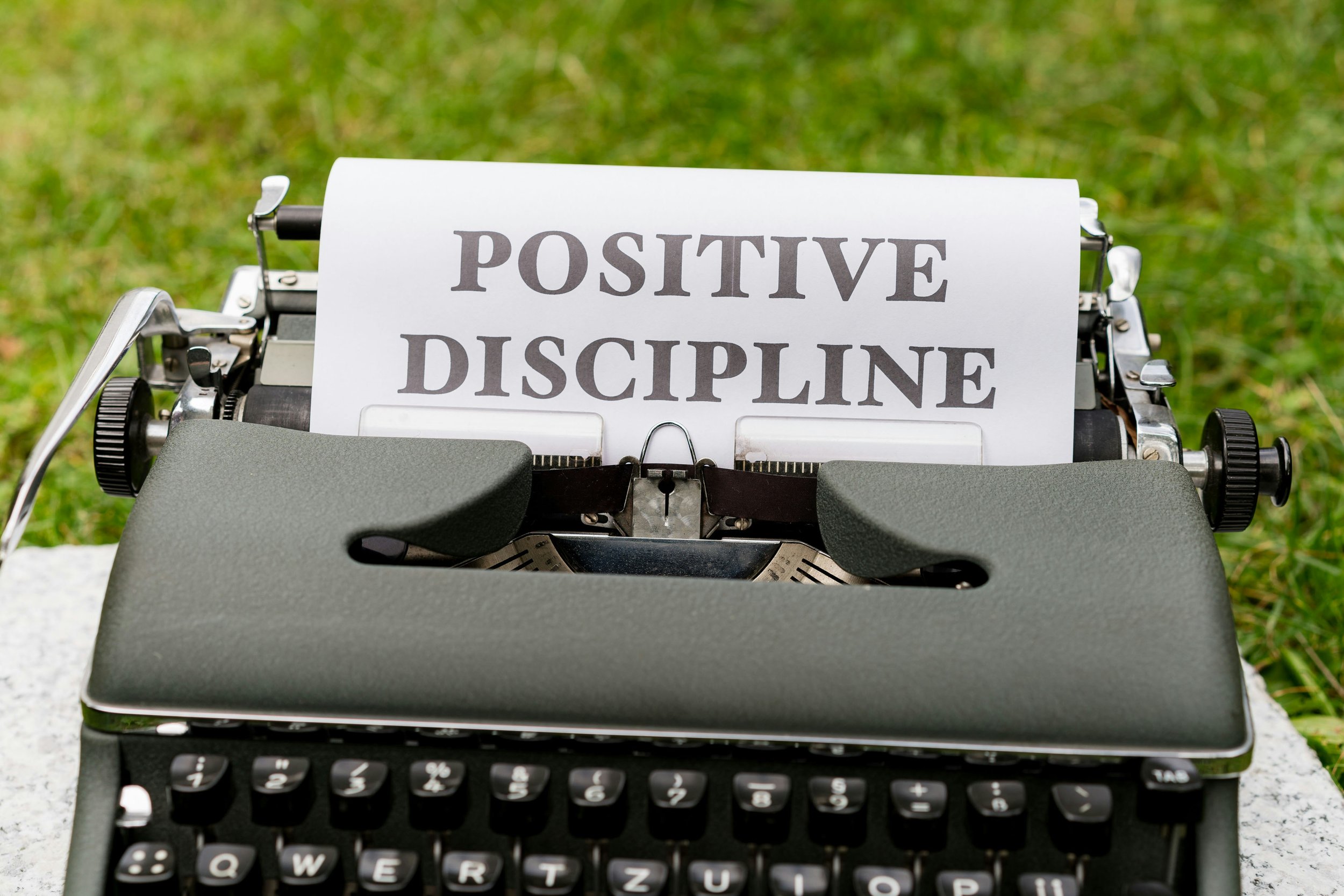 Typewriter with a paper displaying the words 'Positive Discipline' on a grassy surface.