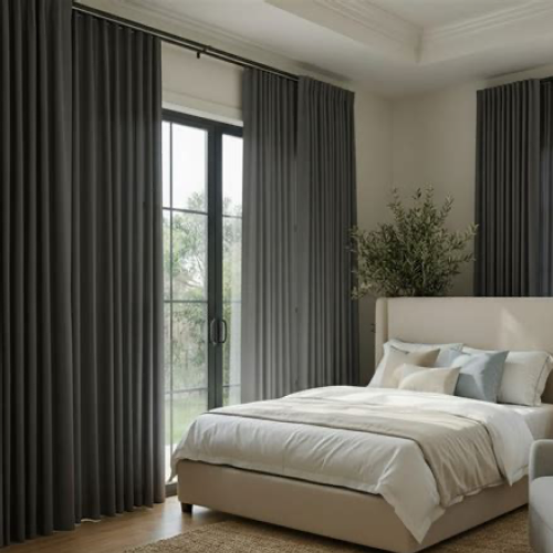 Picture of a bedroom — a beige and light-blue decorated bed with blankets and pillows sits in the foreground. Dark gray blackout curtains hang from the rod to the left and behind the bed.