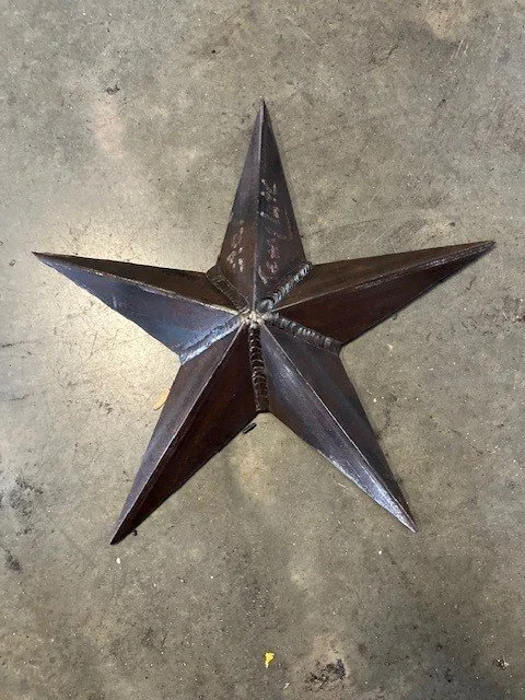 Metal star-shaped sculpture with five points, painted black and brown, on concrete floor.