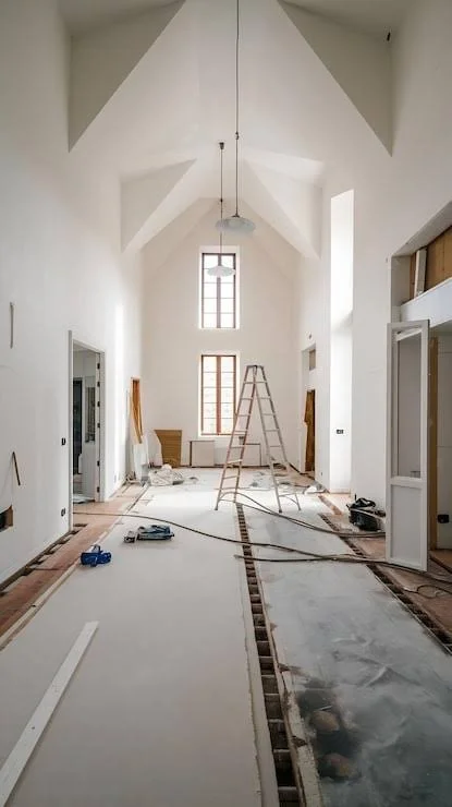 Interior of a church or hall under renovation with construction tools, ladder, and exposed flooring.