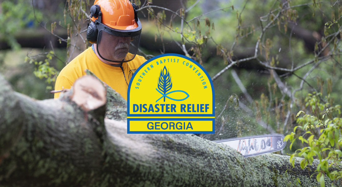 A man wearing an orange helmet and yellow shirt is cutting a fallen tree with a chainsaw in a forest. There is a logo in the center that says 'Southern Baptist Convention Disaster Relief Georgia'.