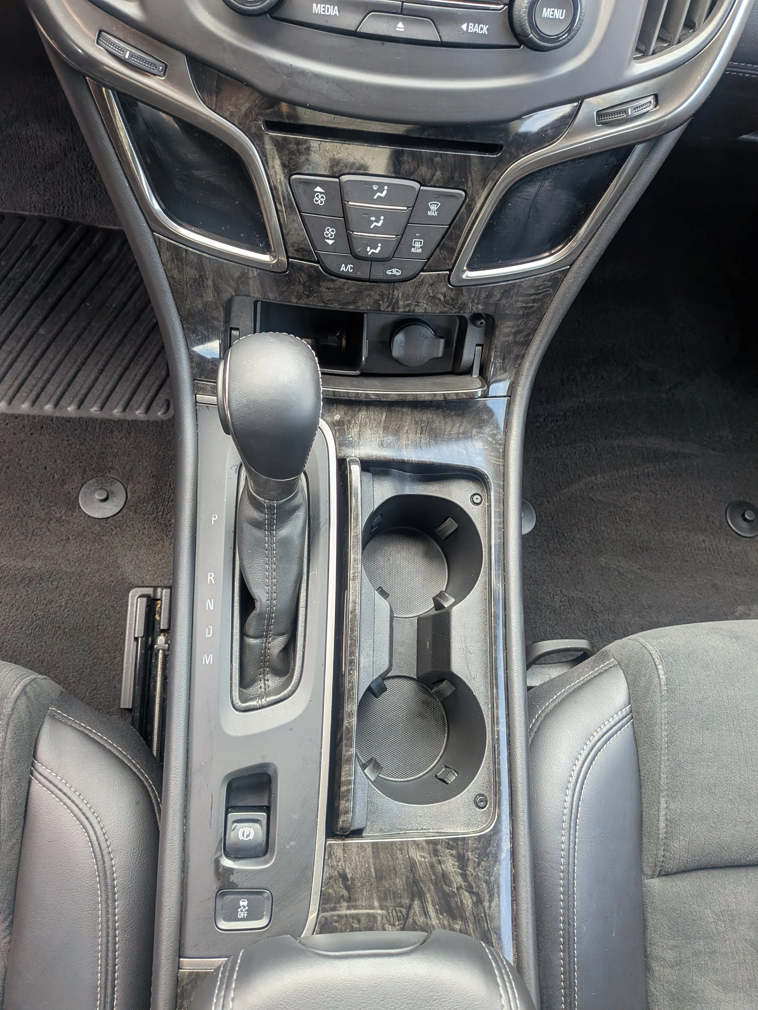 Center console of a car showing gear shift, cup holders, and climate control buttons.