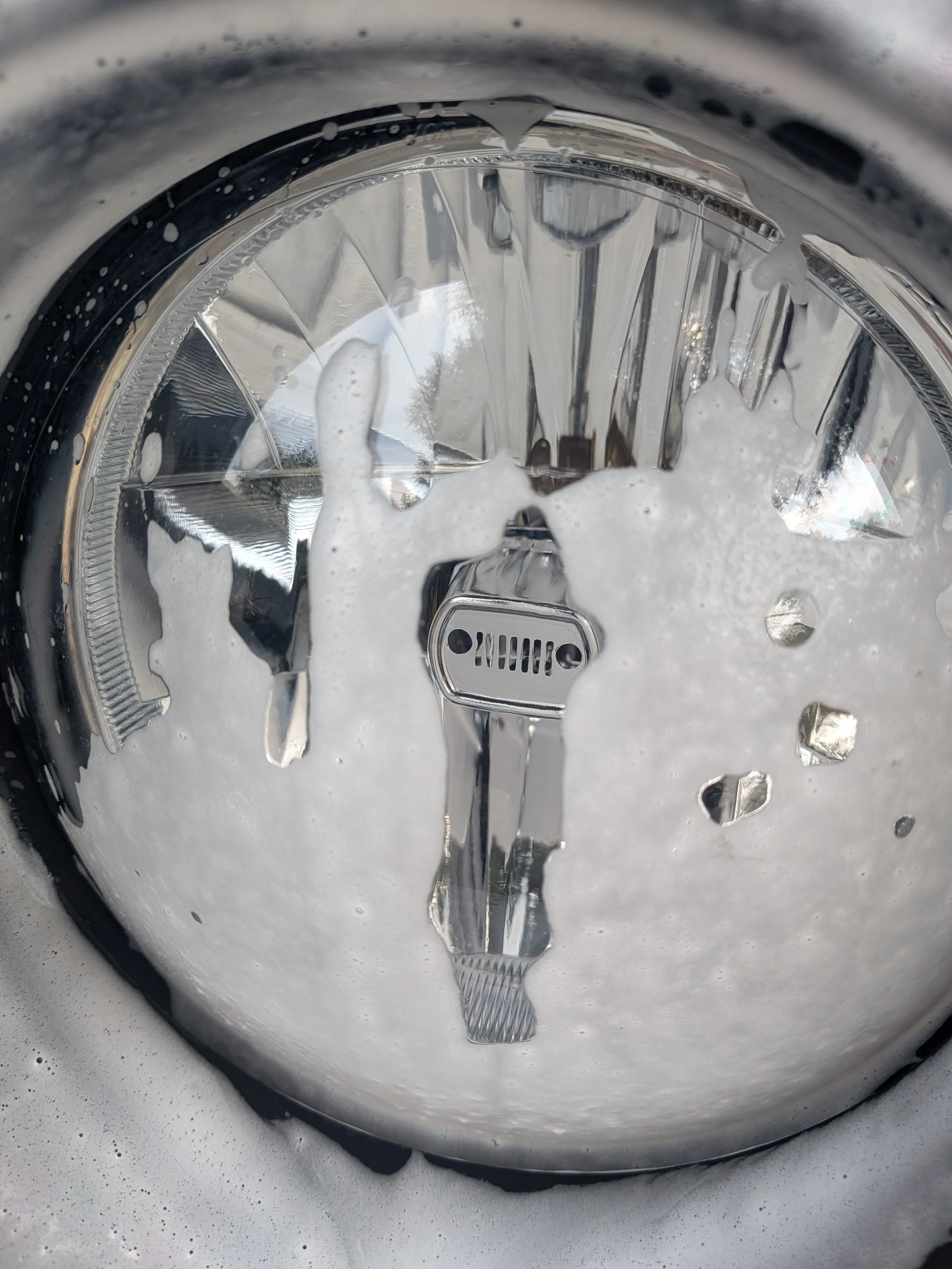 Close-up of a Jeep headlight covered in soap from a foam cannon.