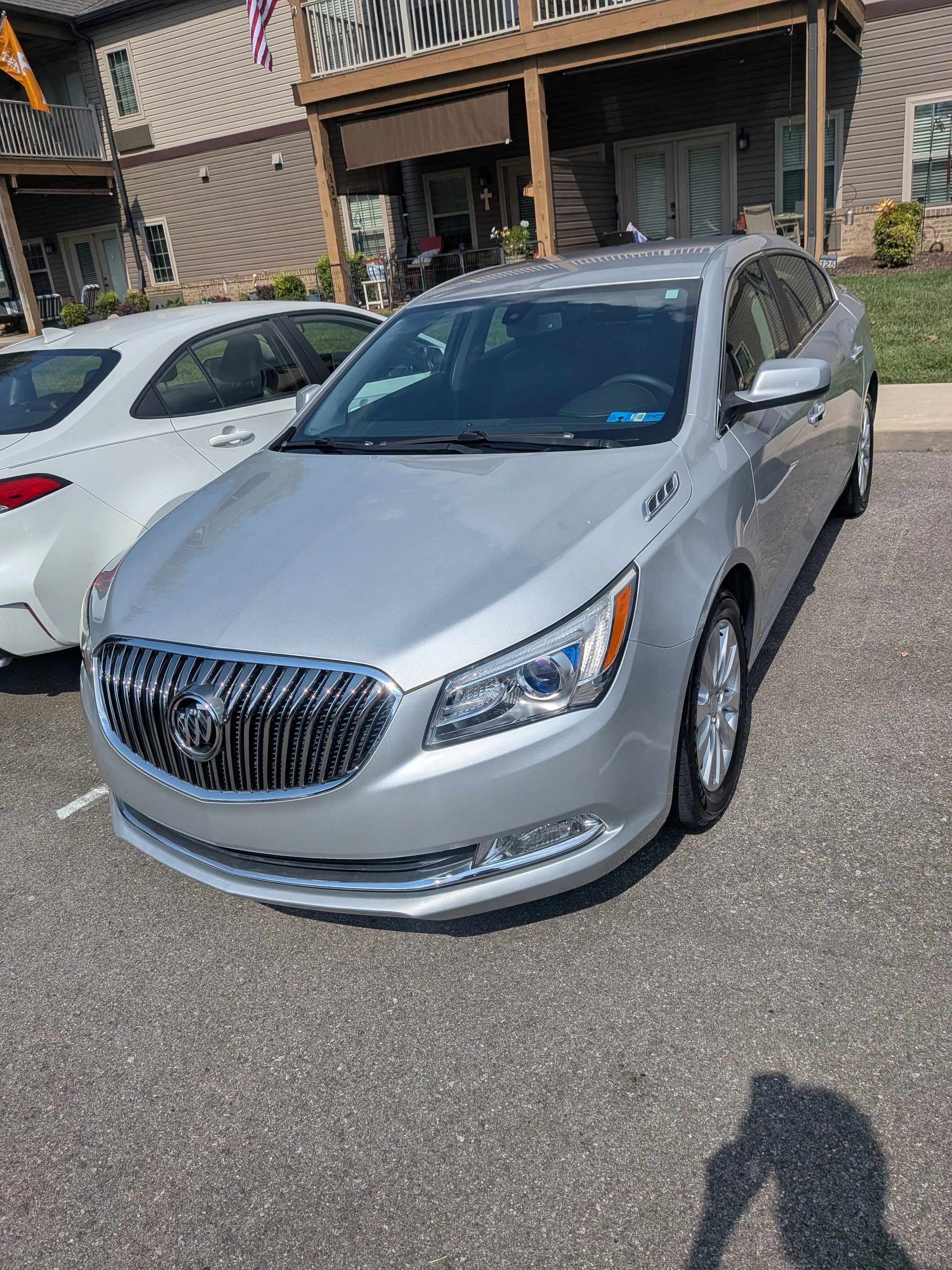 A silver sedan car parked next to a white car in a residential parking lot with apartment buildings and balconies in the background.