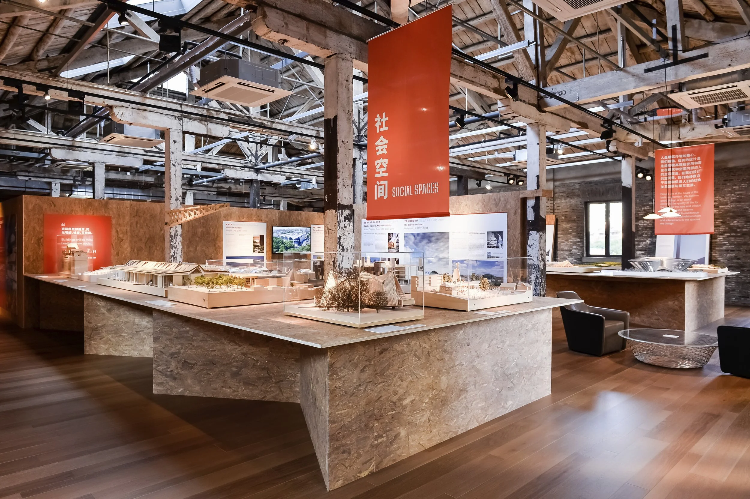 Main room of the exhibition with several models resting on tables and an orange banner indicating the specific section in dual language.