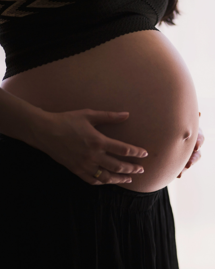 Close-up of a pregnant woman's abdomen being gently cradled with both hands.