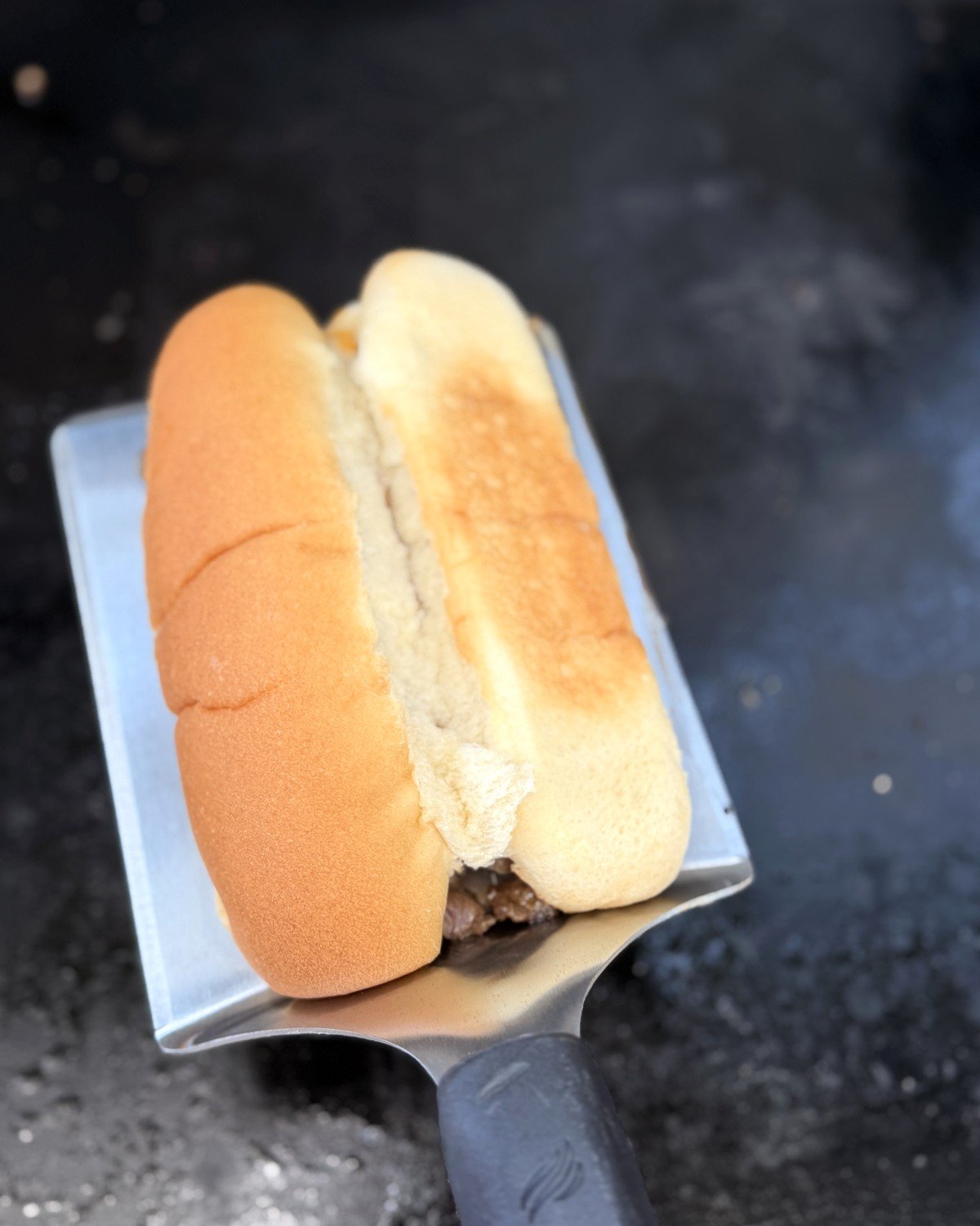 Toasted hoagie roll flipped onto a spatula over steak