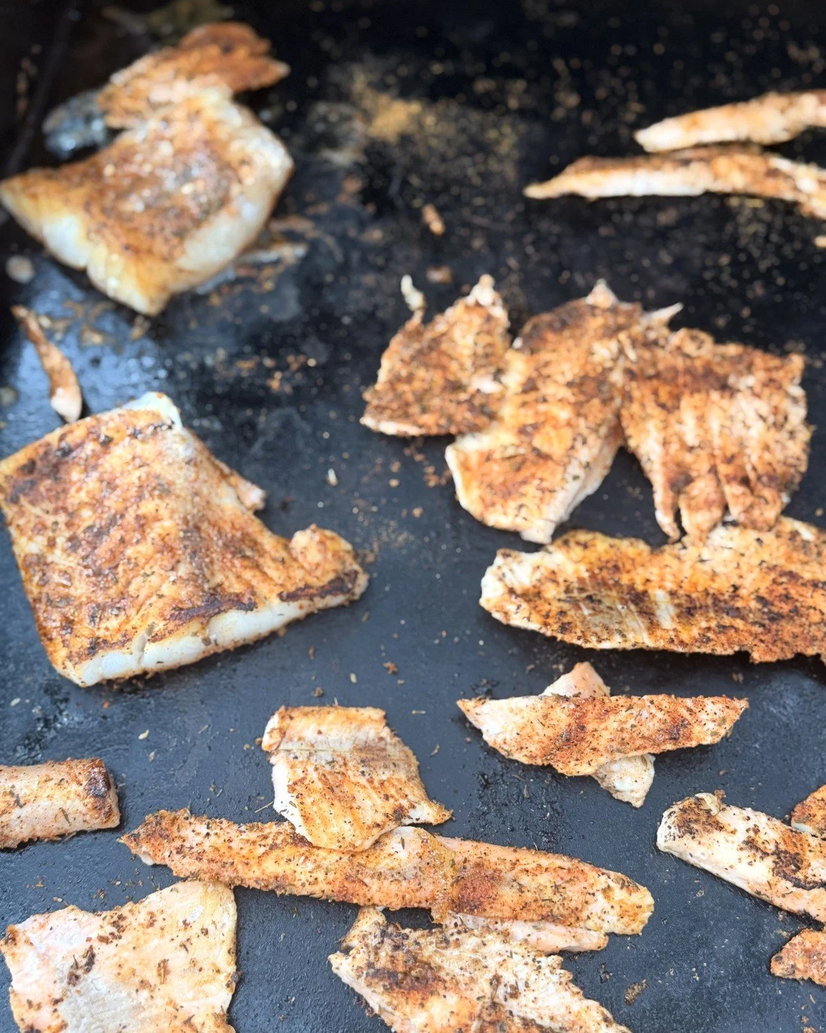 Blackened fish fillets cooking on a griddle