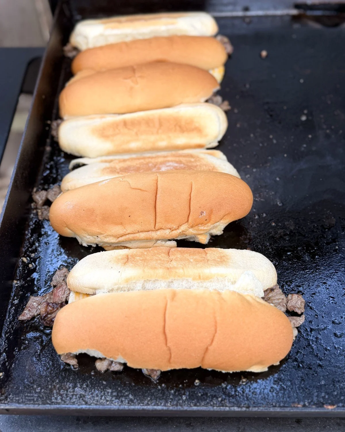 Hoagie rolls resting on piles of steak on a Blackstone griddle