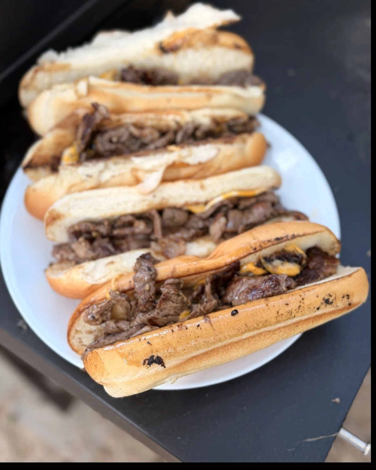 Philly cheesesteaks on hoagie rolls on a white platter
