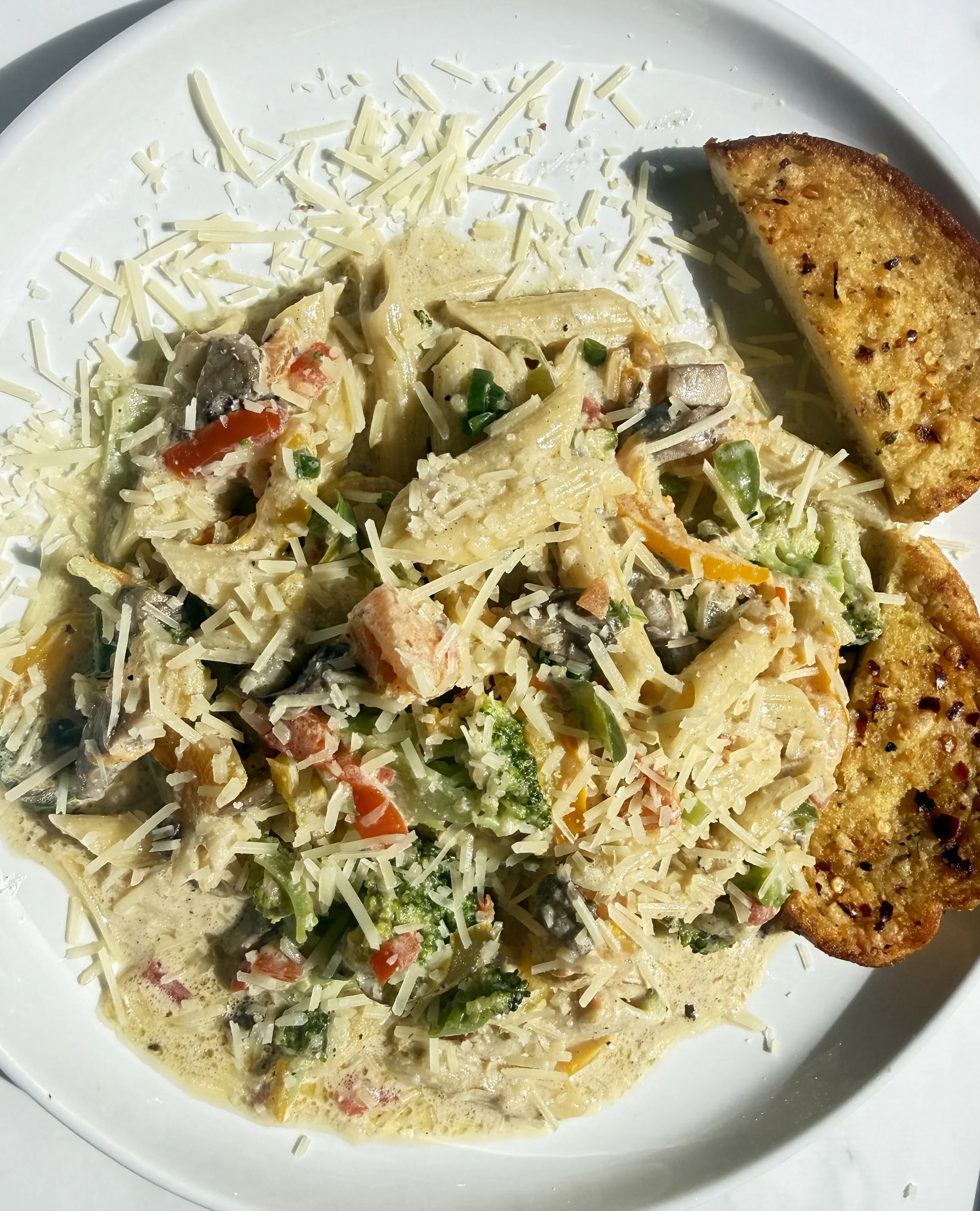 A plate of creamy vegetable soup topped with shredded cheese, with a toasted garlic bread slice on the side.