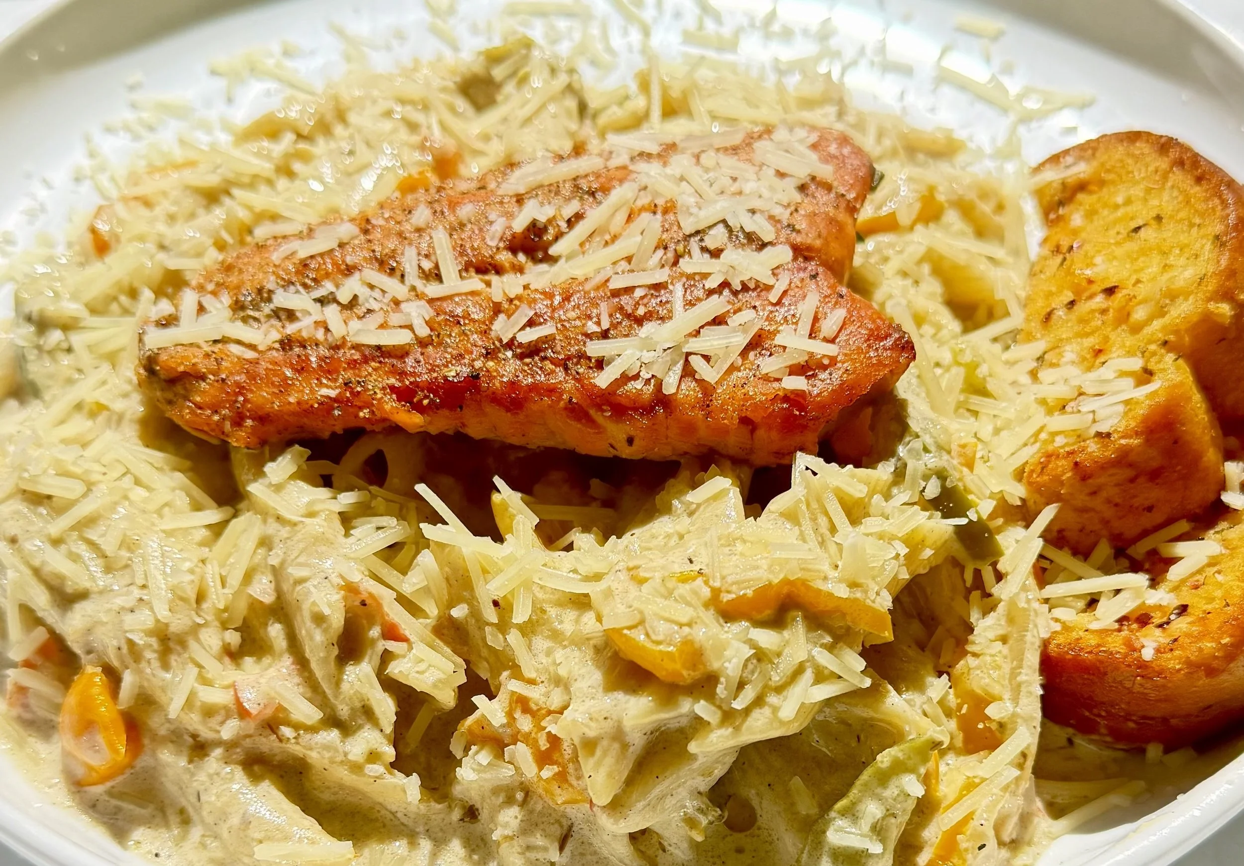 Close-up of a dish with baked fish topped with shredded cheese, accompanied by creamy potato salad with carrots.