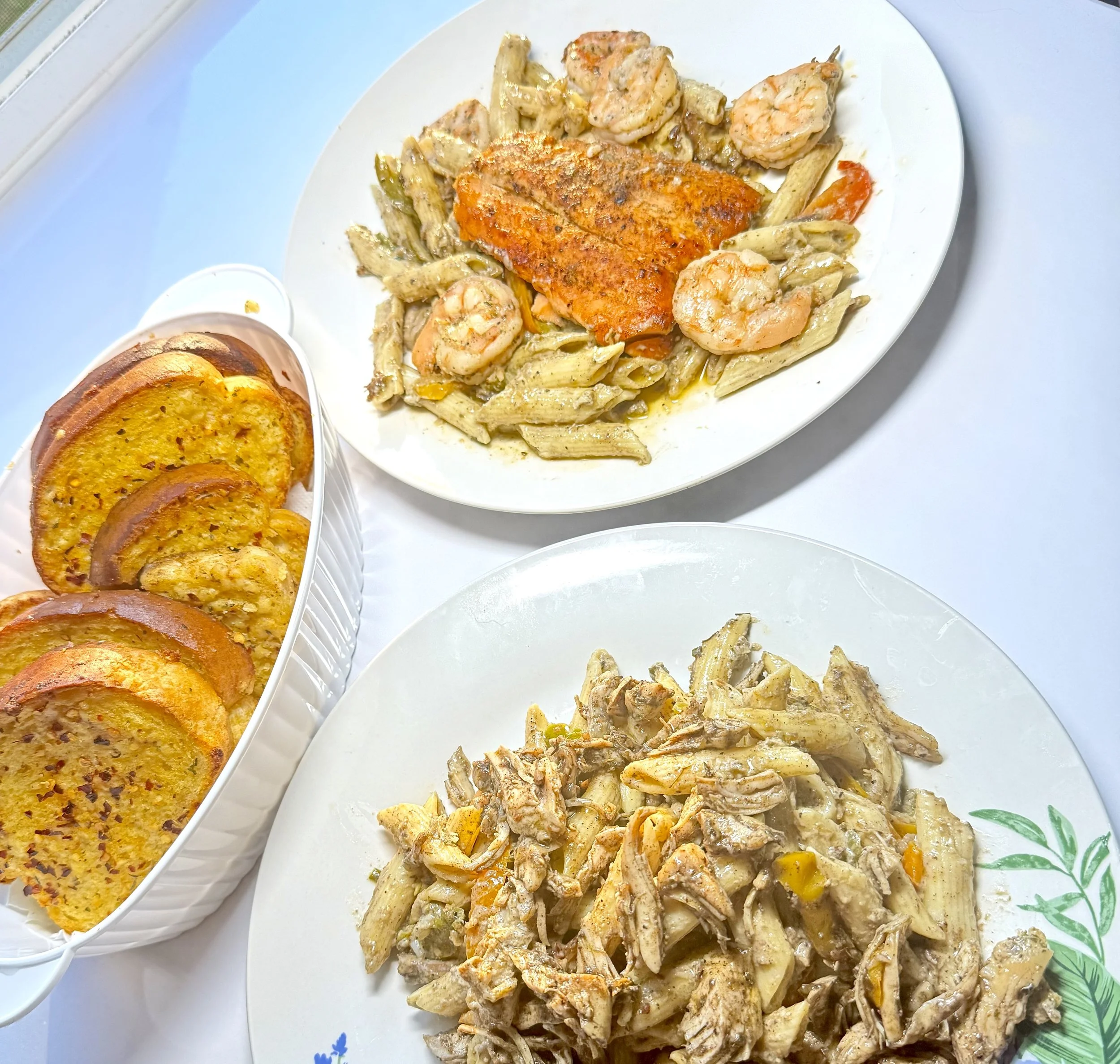 Plate with cooked pasta, shrimp, and grilled chicken, served with a side of fried plantains.