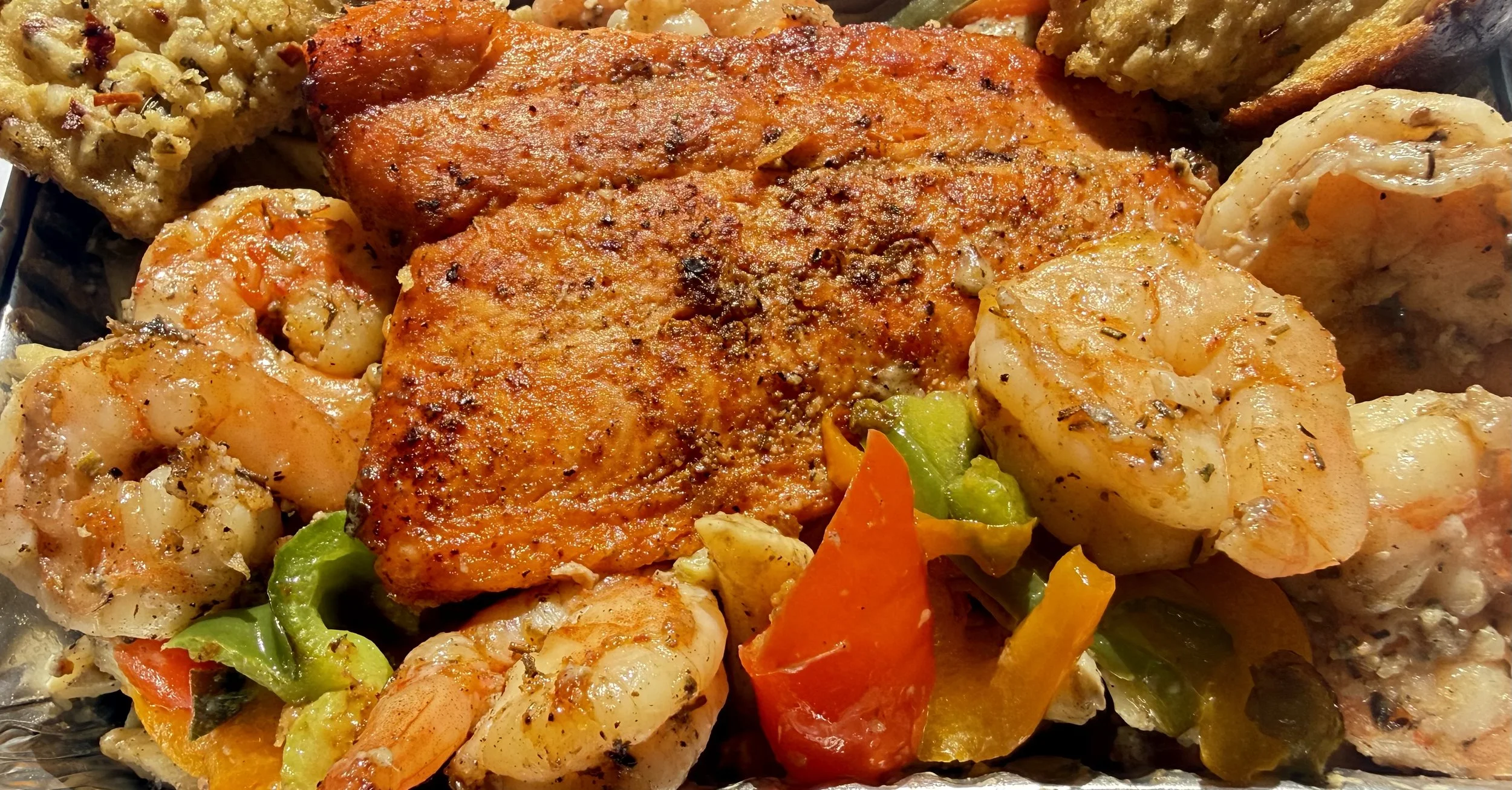 Close-up of cooked seafood, including lobster tail and shrimp, with roasted vegetables like bell peppers.