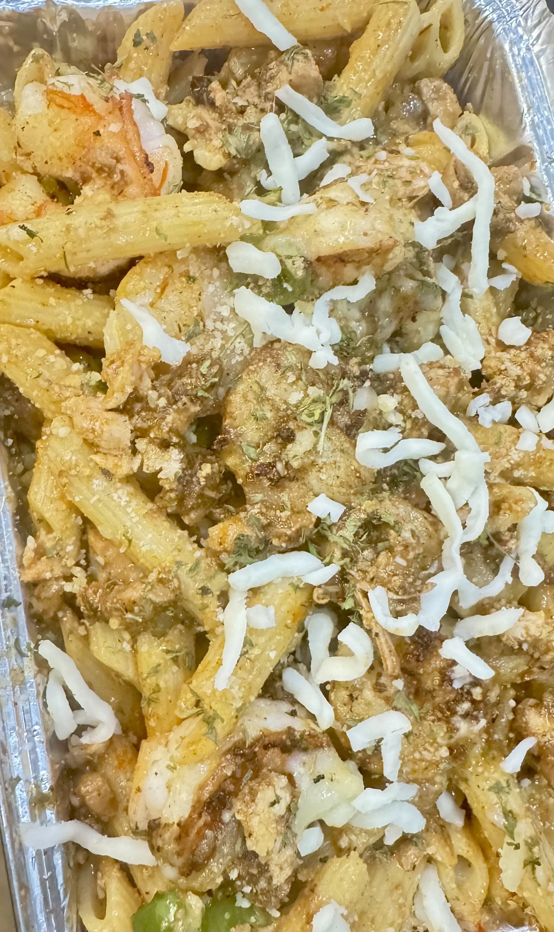 Close-up of a baked pasta dish with penne, cauliflower, shredded cheese, and herbs.