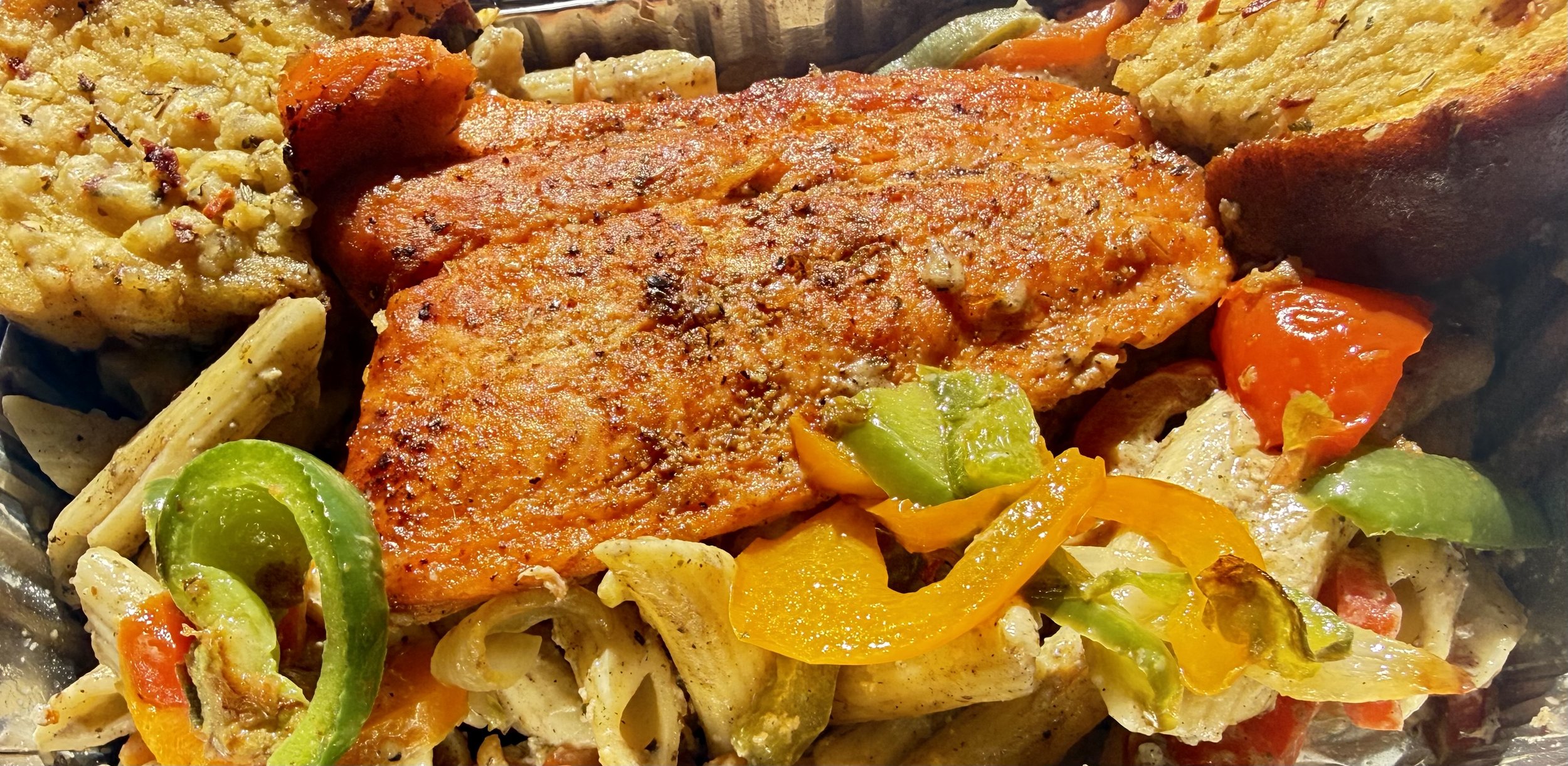 Close-up of cooked salmon fillet with a golden crust surrounded by roasted vegetables including bell peppers, zucchini, and cauliflower.