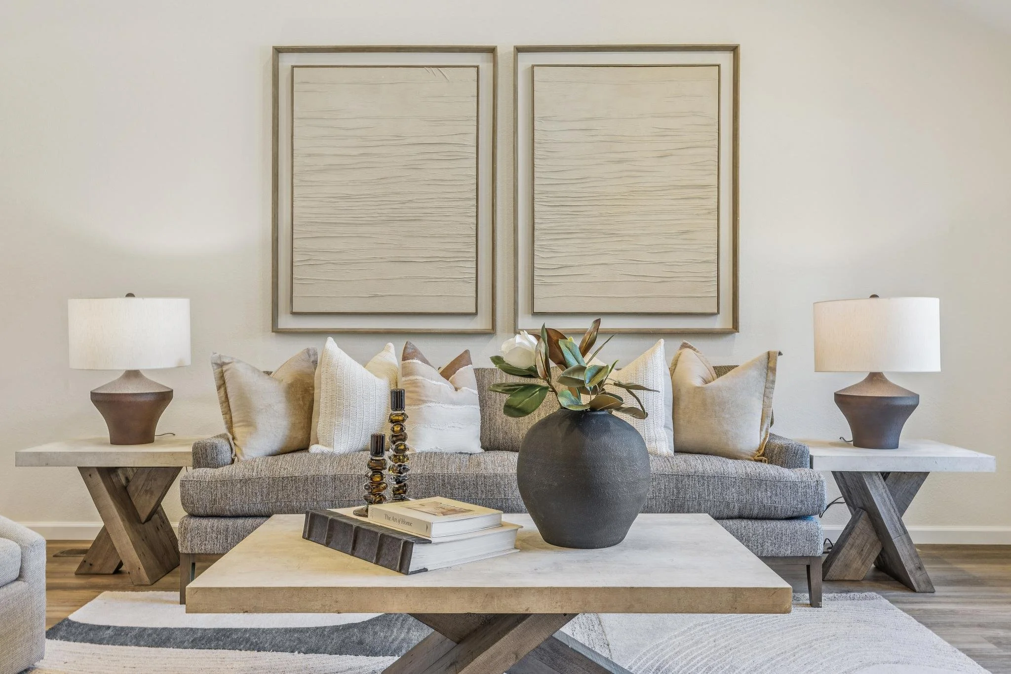 Living room with two beige lamps on side tables, a gray sofa with beige and white pillows, a black vase with white flowers, and two large framed art pieces on the wall.